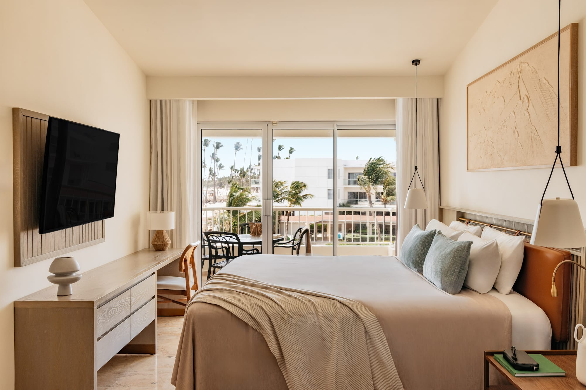 Contemporary hotel room with balcony, king bed, and tropical resort view.
