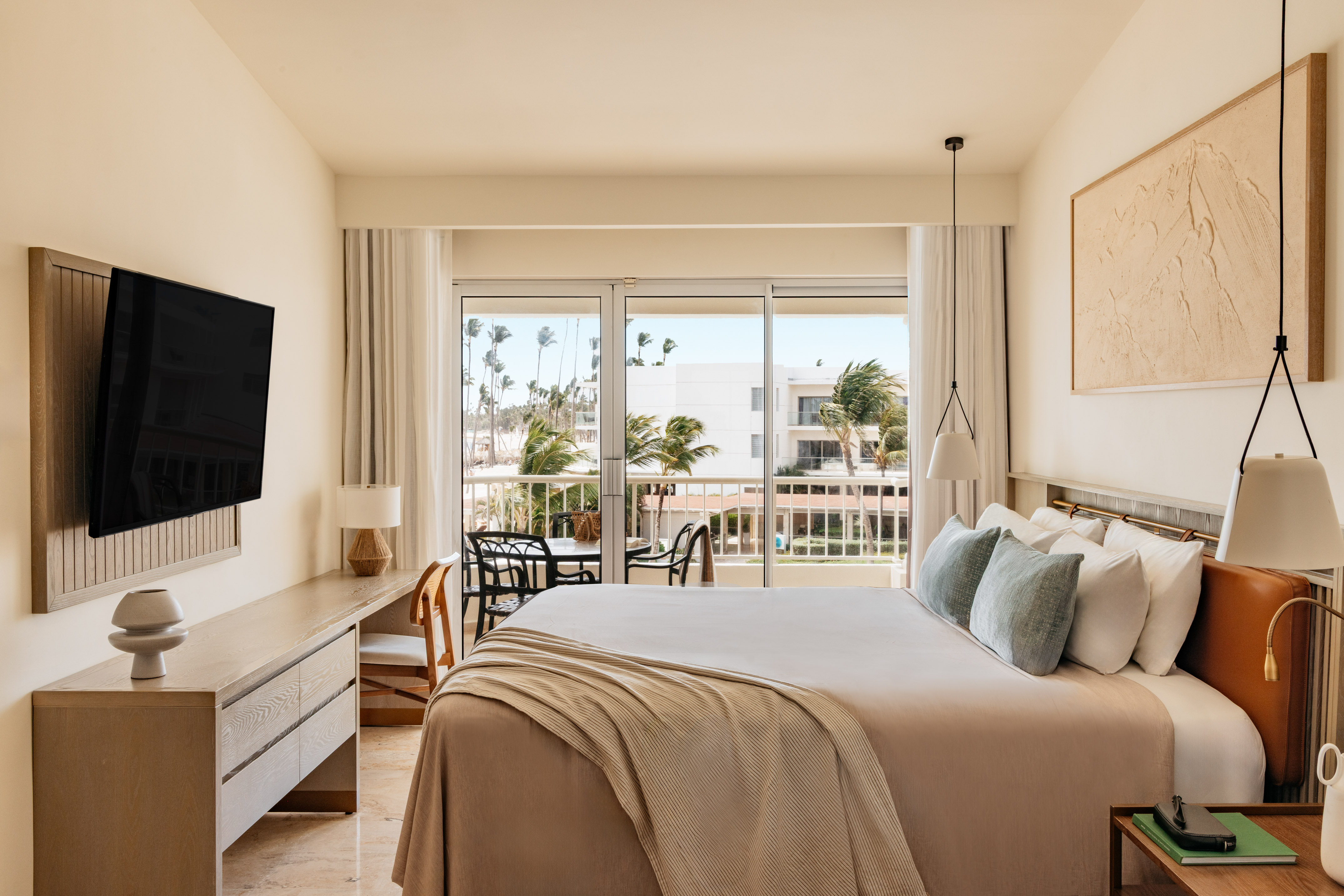 Contemporary hotel room with balcony, king bed, and tropical resort view.