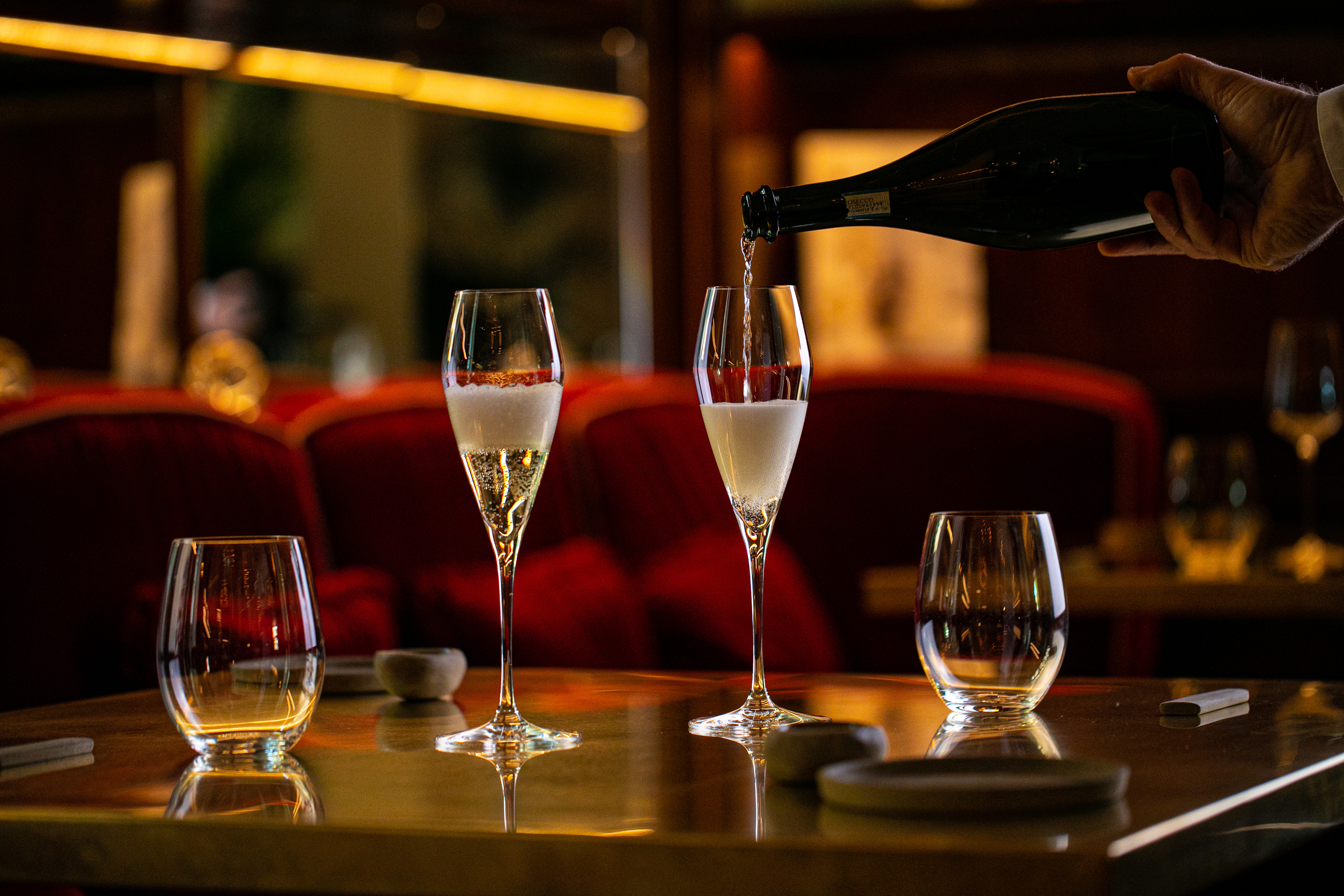Pouring Prosecco into flutes at an elegant restaurant table.