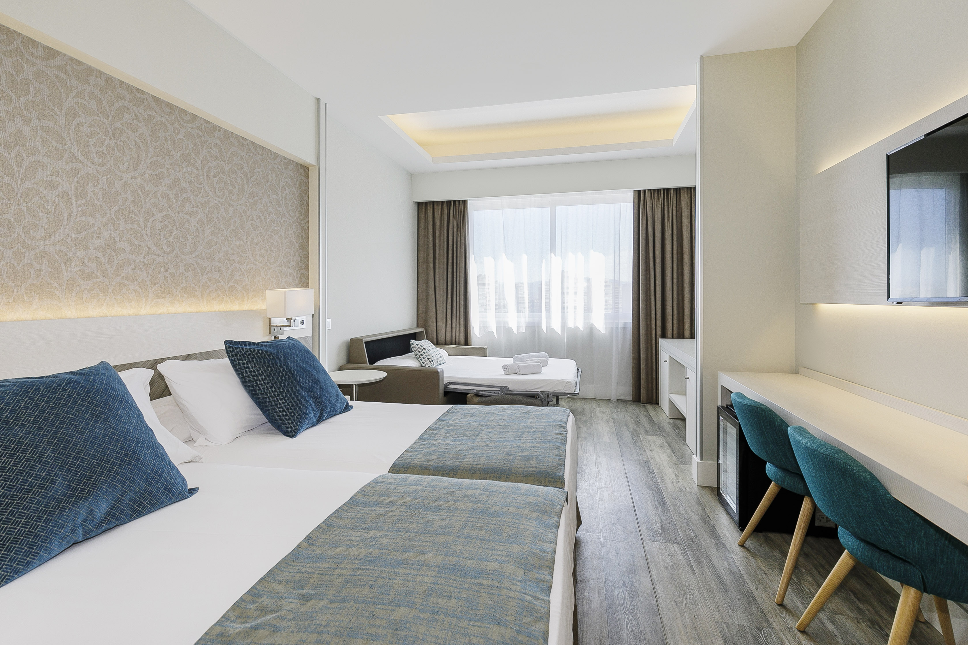 Spacious hotel room with twin beds, pull-out sofa bed, modern desk, and TV.