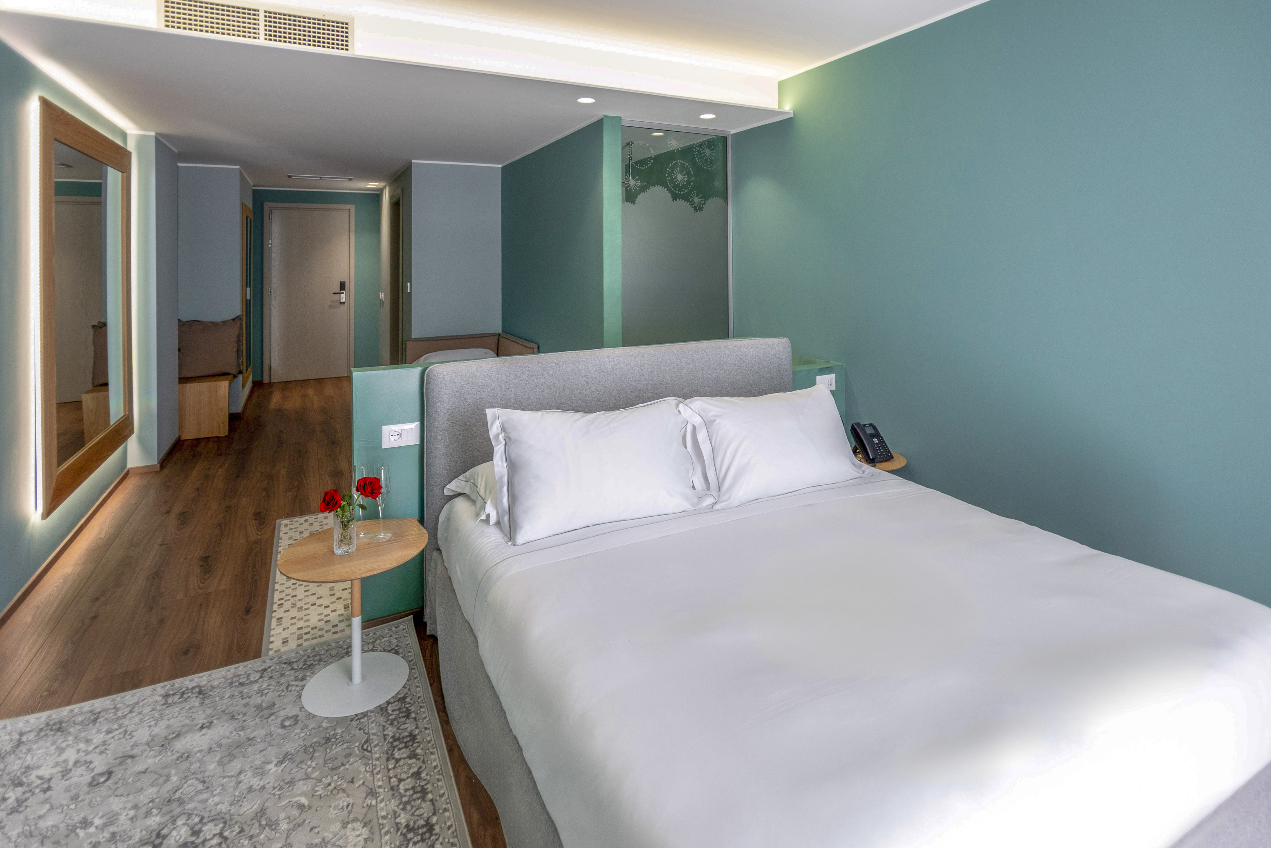 Chic hotel bedroom with king bed, teal accent walls, wood floor, and modern decor.