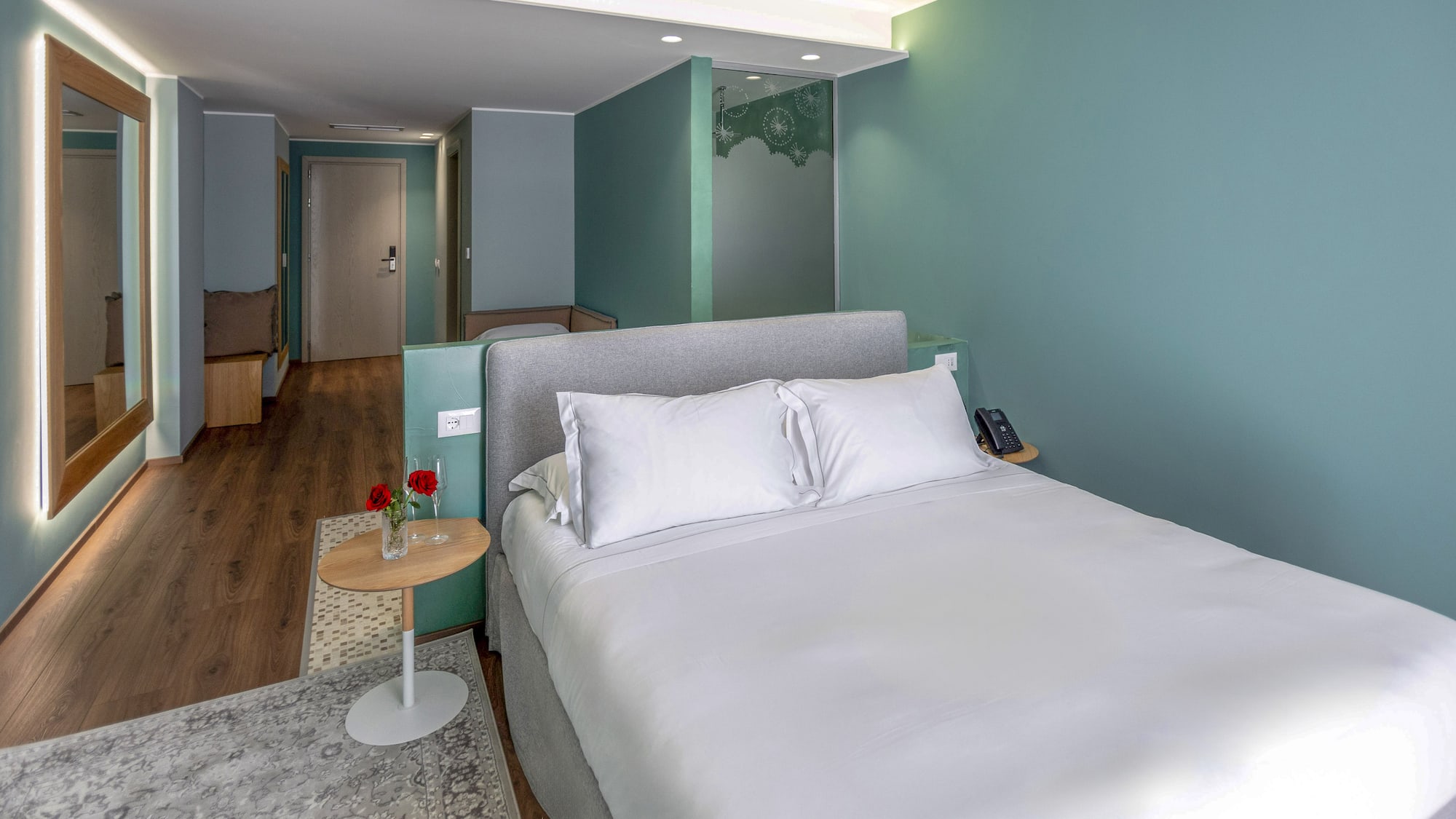Chic hotel bedroom with king bed, teal accent walls, wood floor, and modern decor.