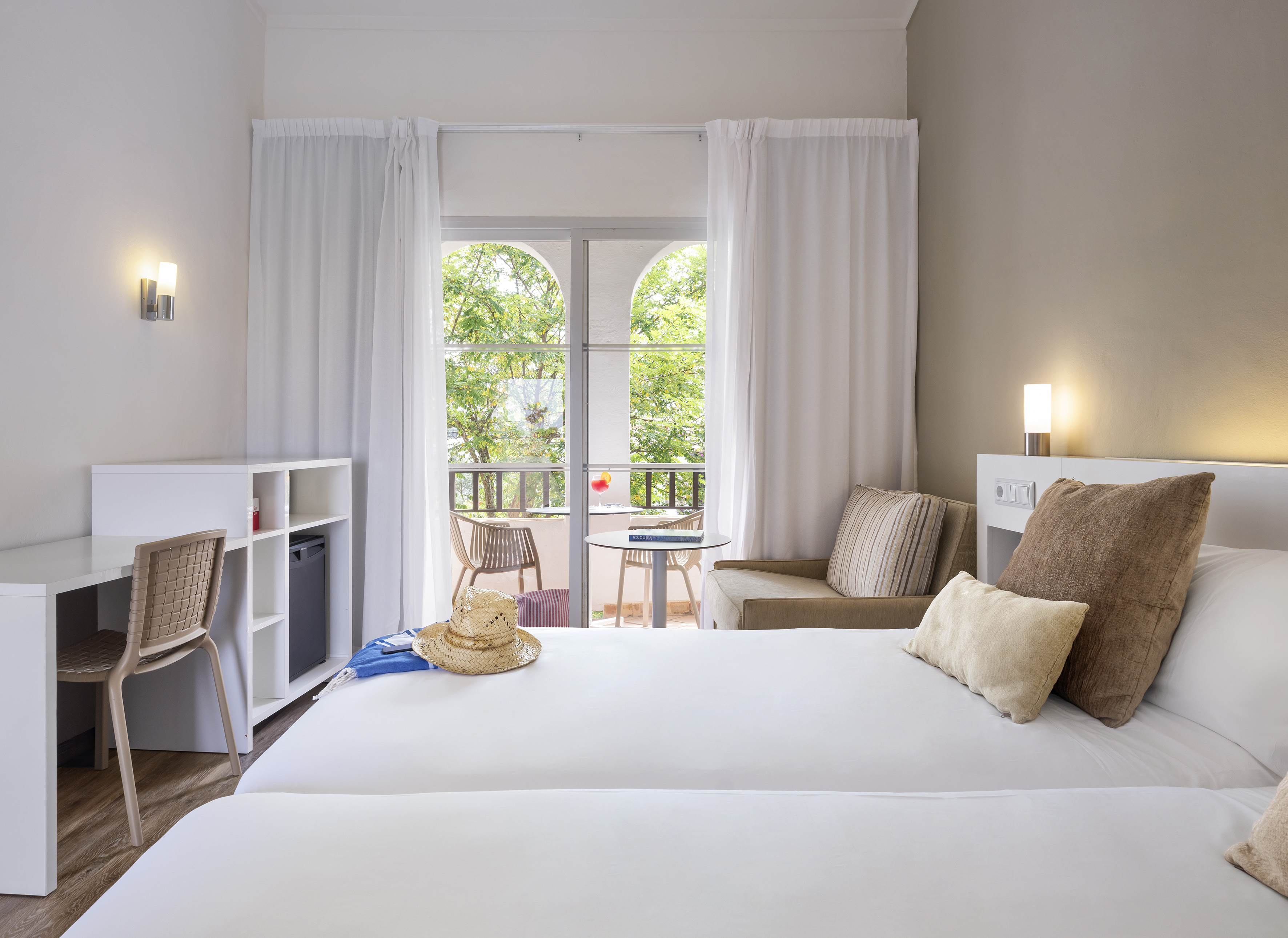 Modern hotel room with twin beds, balcony, desk, and green tree view.