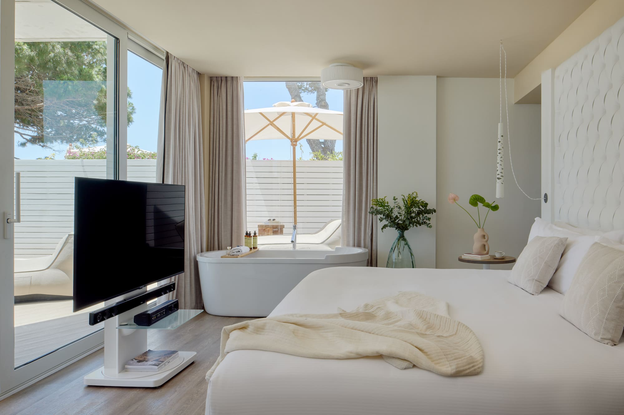 Modern hotel suite with freestanding tub, private patio, white decor, and TV.