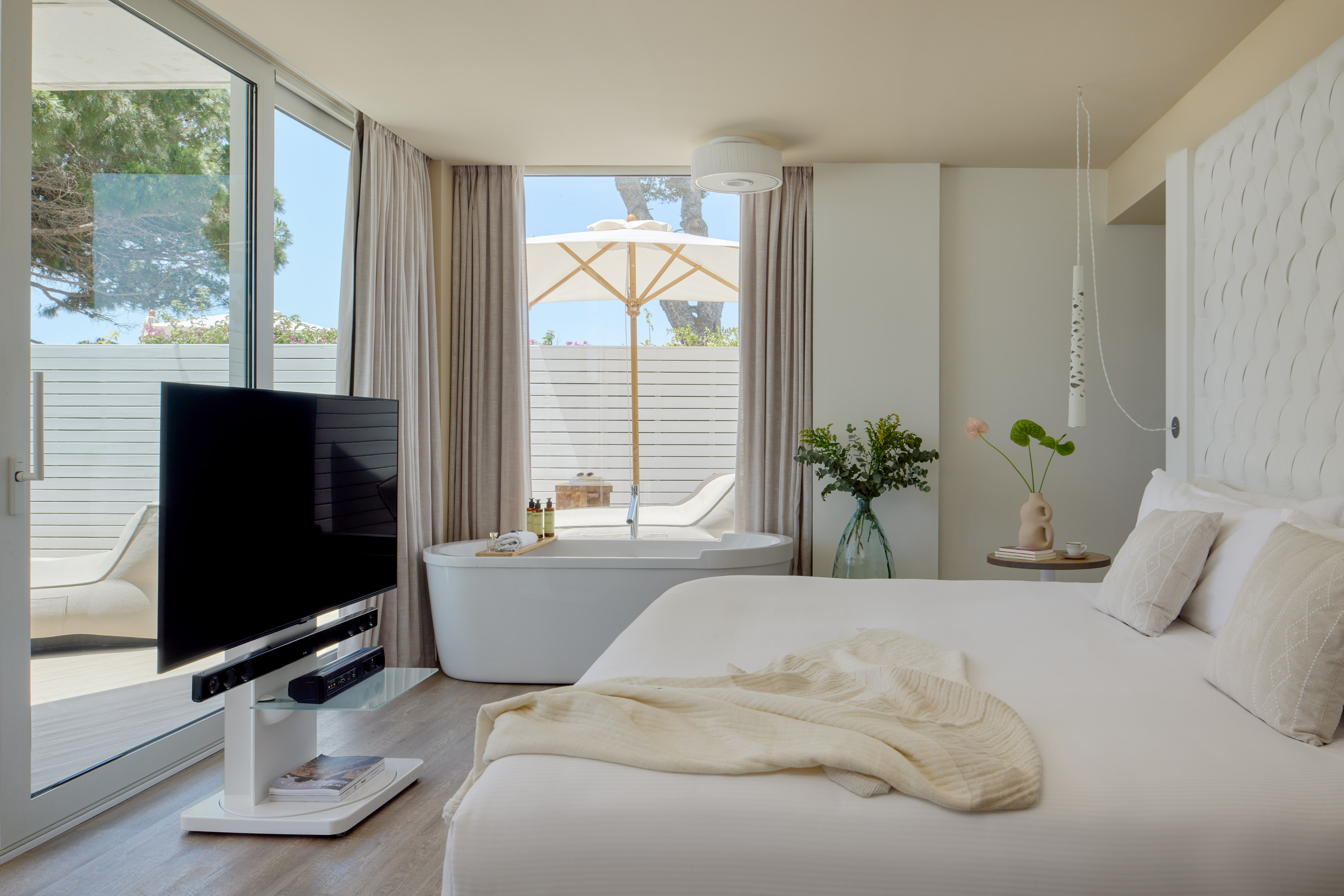 Modern hotel suite with freestanding tub, private patio, white decor, and TV.