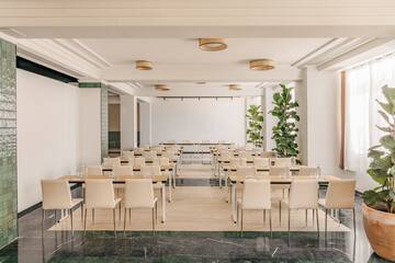 Modern corporate meeting room with wood tables, beige chairs, and potted plants.