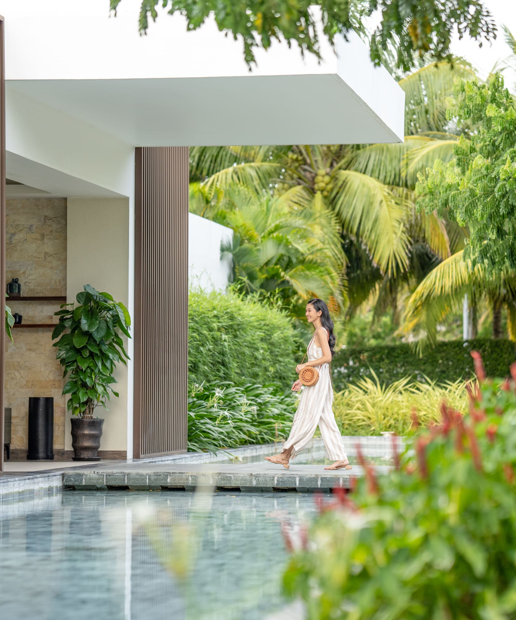 Woman walks past YHI Spa entrance beside tranquil pool in tropical resort.