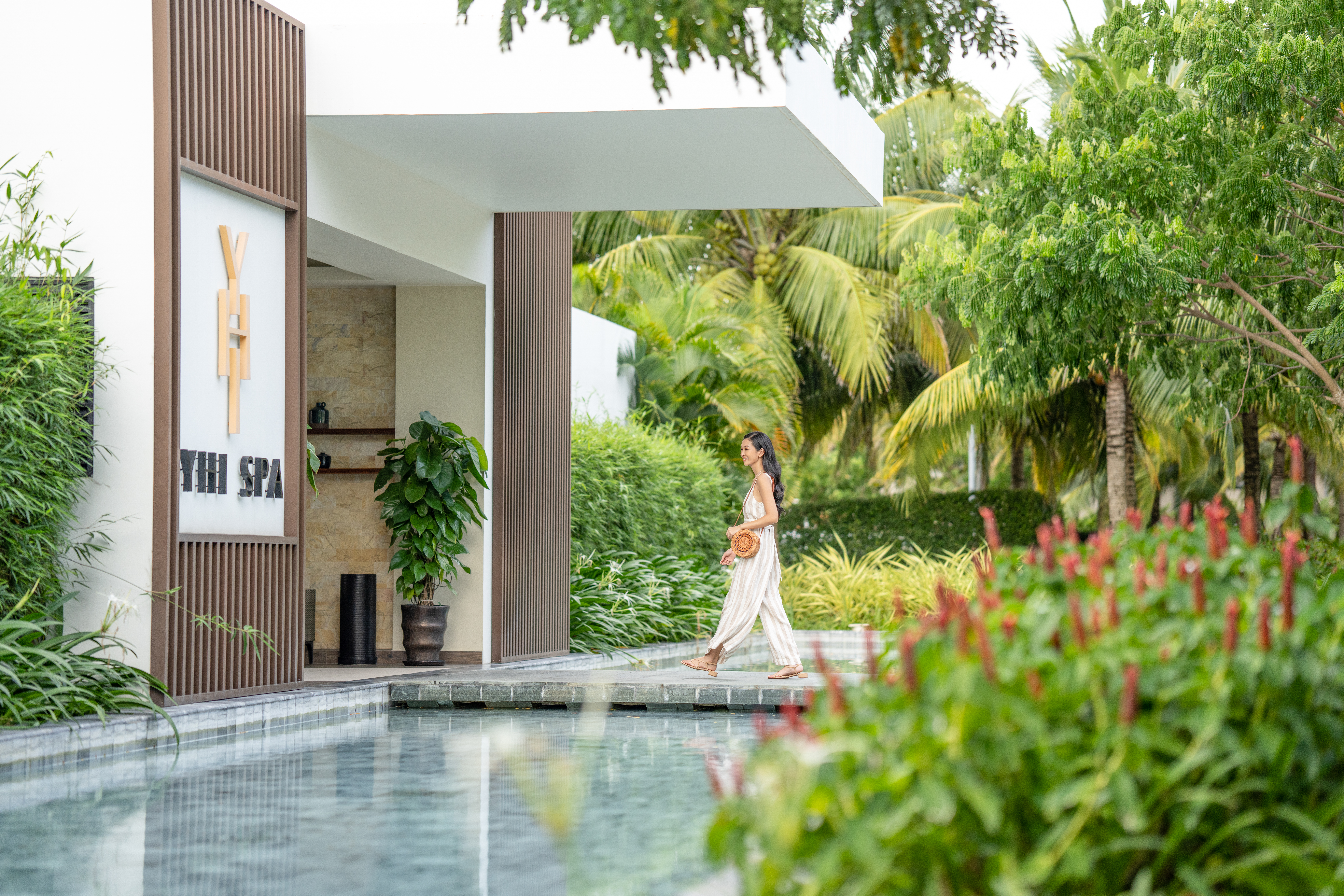 Woman walking past YHI Spa entrance and reflective pool in a tropical resort.