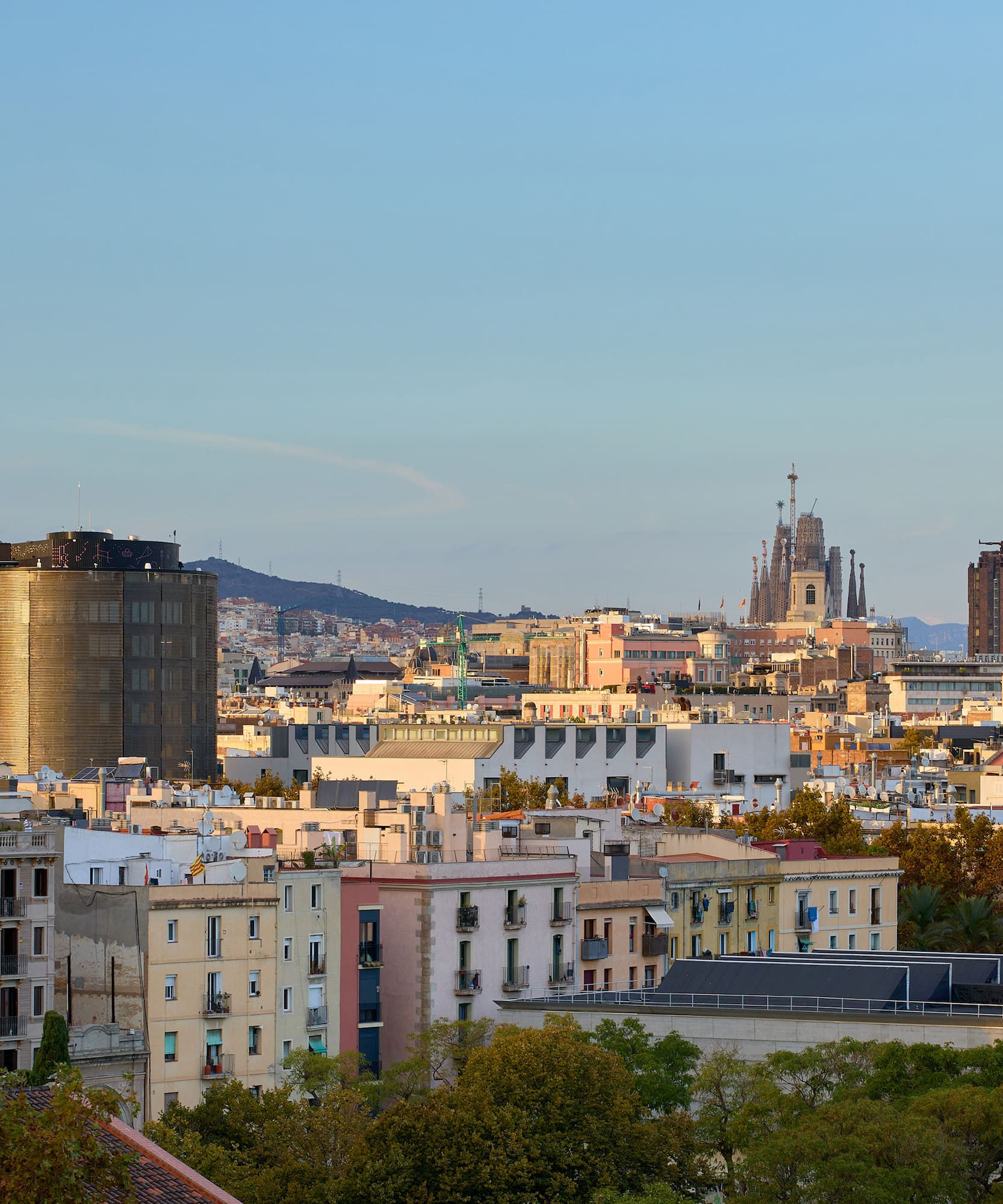 Vista panorámica de Barcelona con Sagrada Familia, edificios y montañas al atardecer.