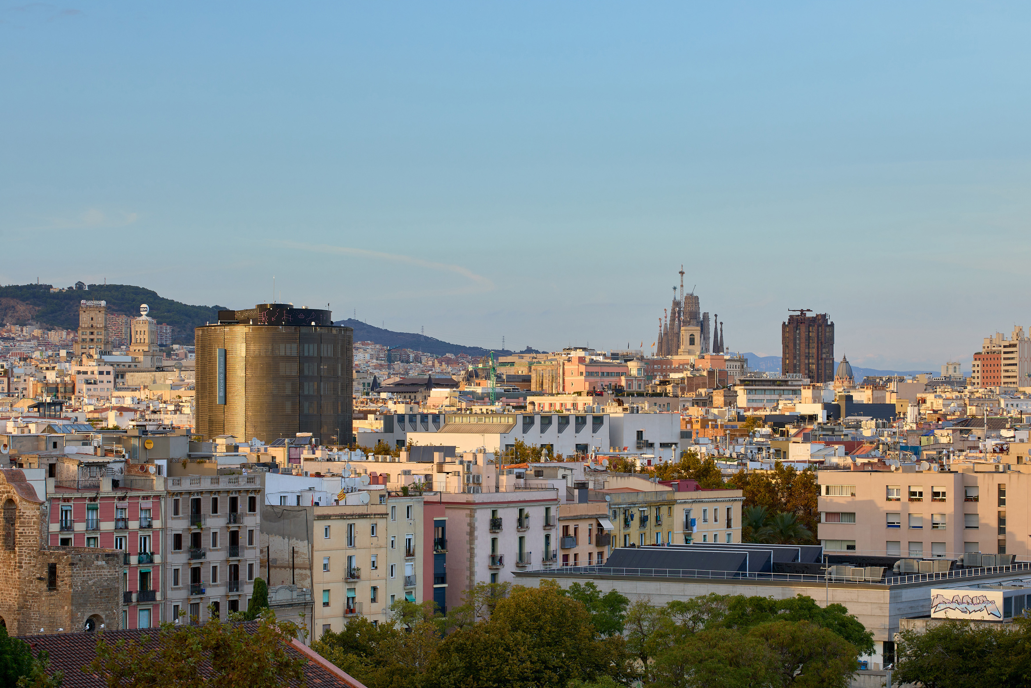 Vista panorámica de Barcelona con Sagrada Familia, edificios y montañas al atardecer.