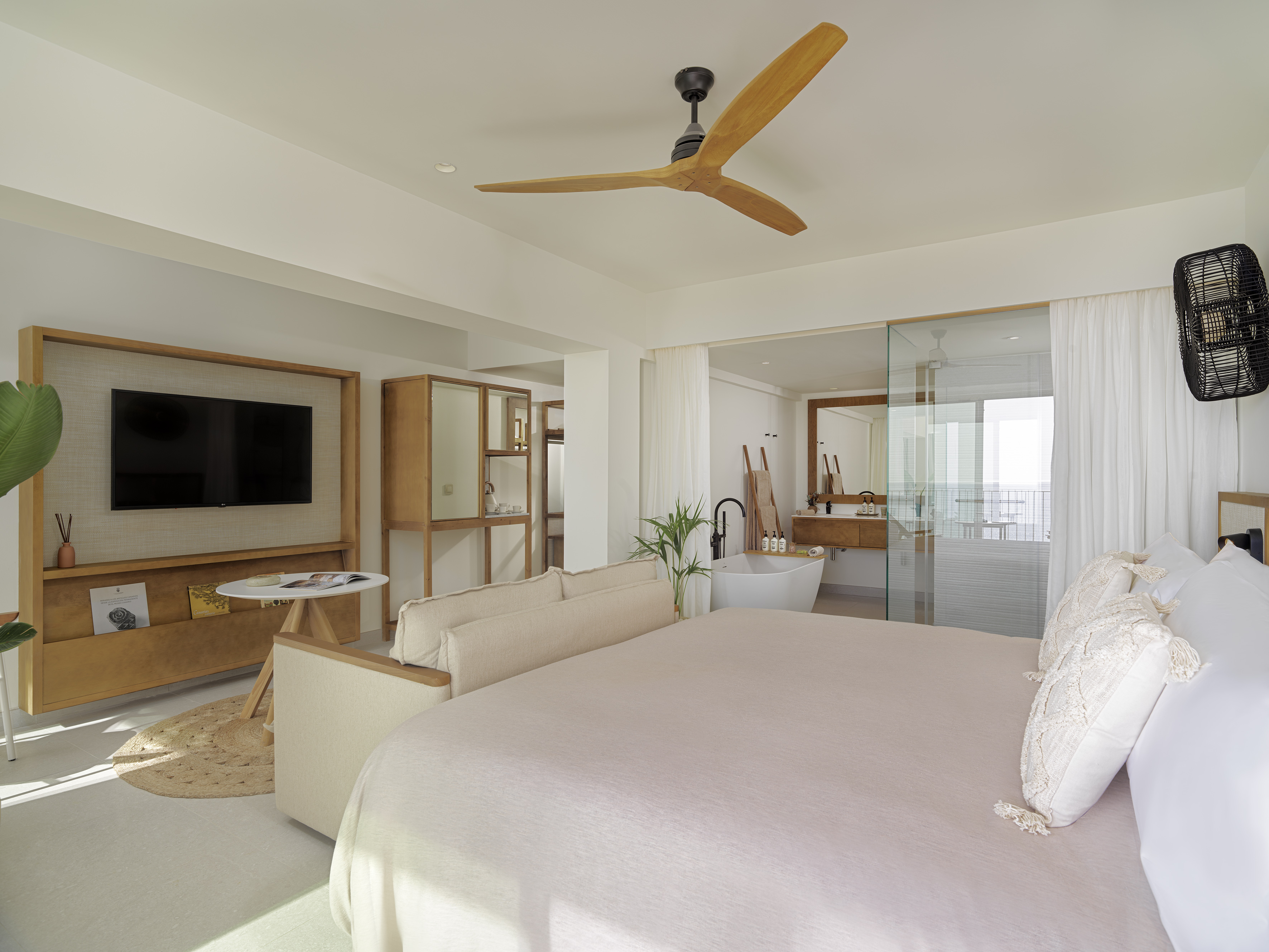 Modern hotel suite with king bed, open-concept bathroom, and wood ceiling fan.