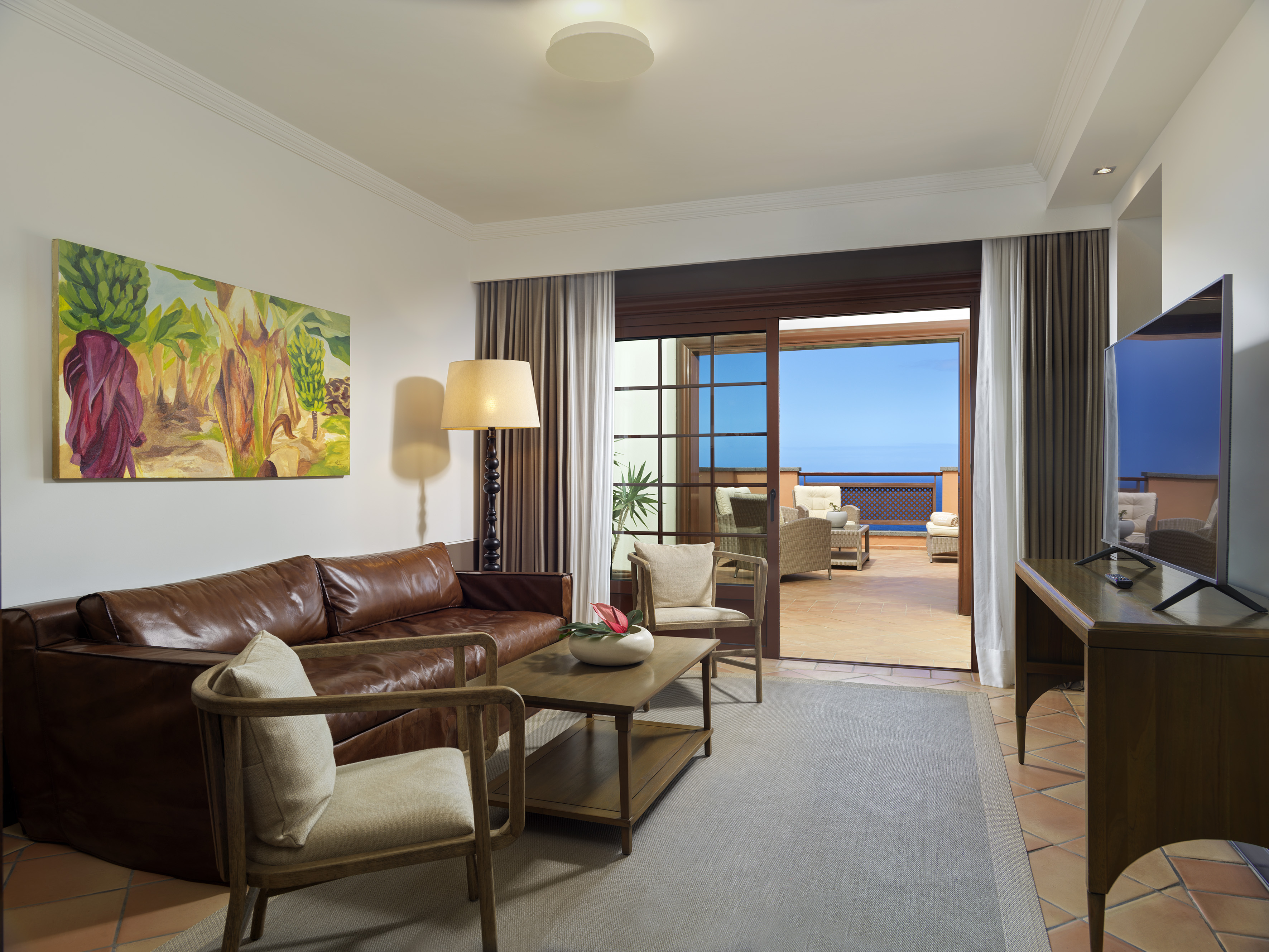 Living room with leather sofa, banana tree art, and ocean view terrace.