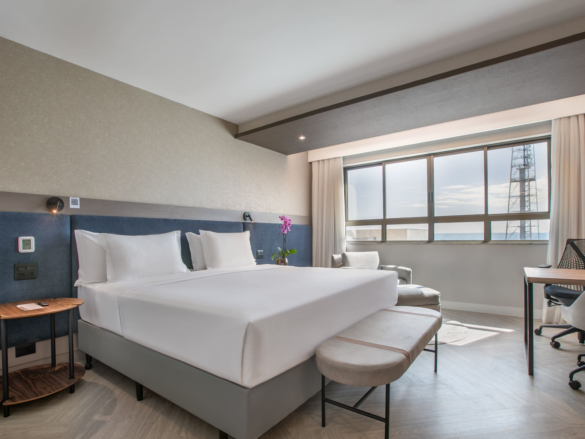 Modern hotel guest room with king bed, city view, and work desk.