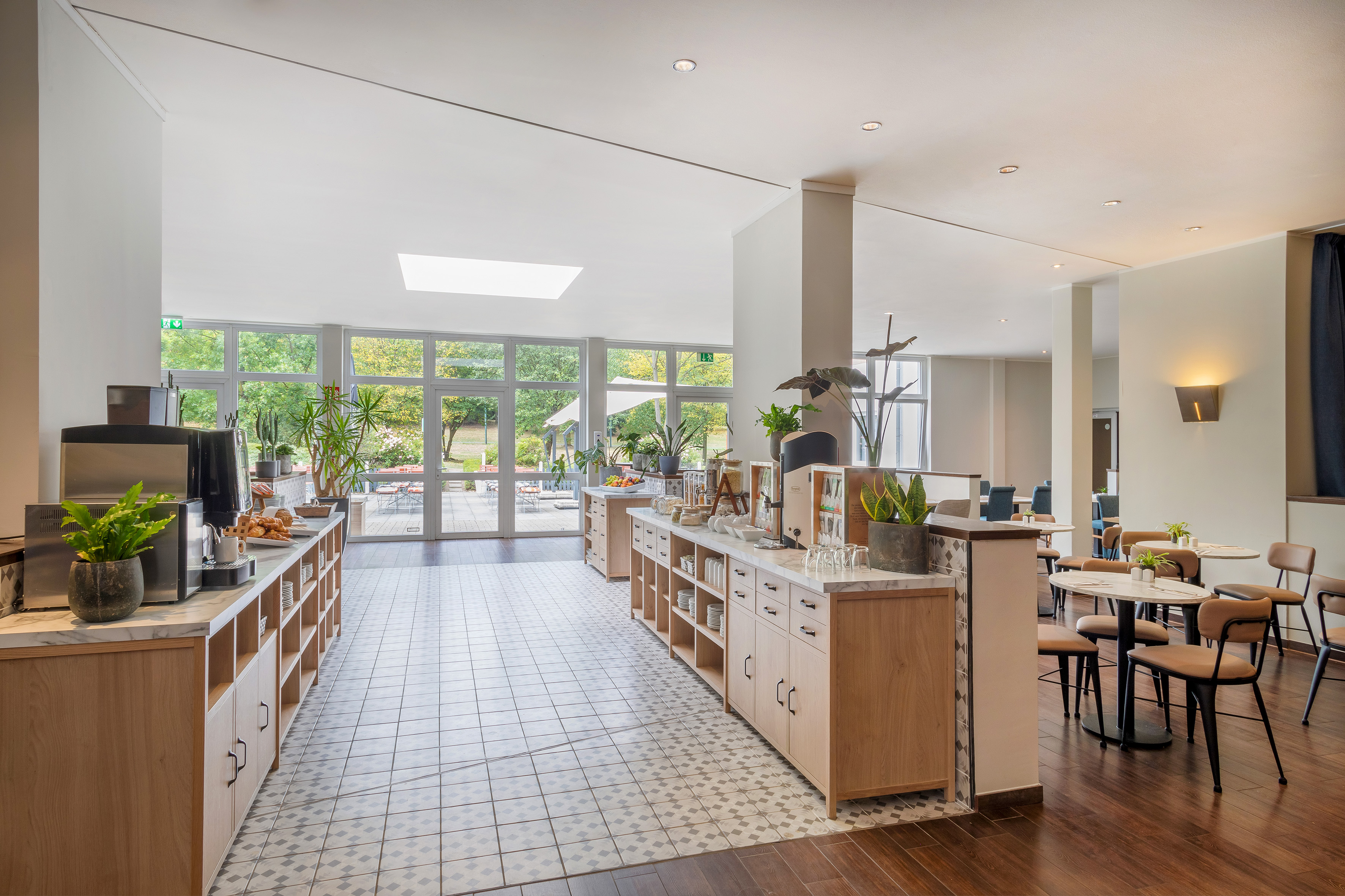 Bright hotel breakfast buffet with modern decor, seating, and garden views.