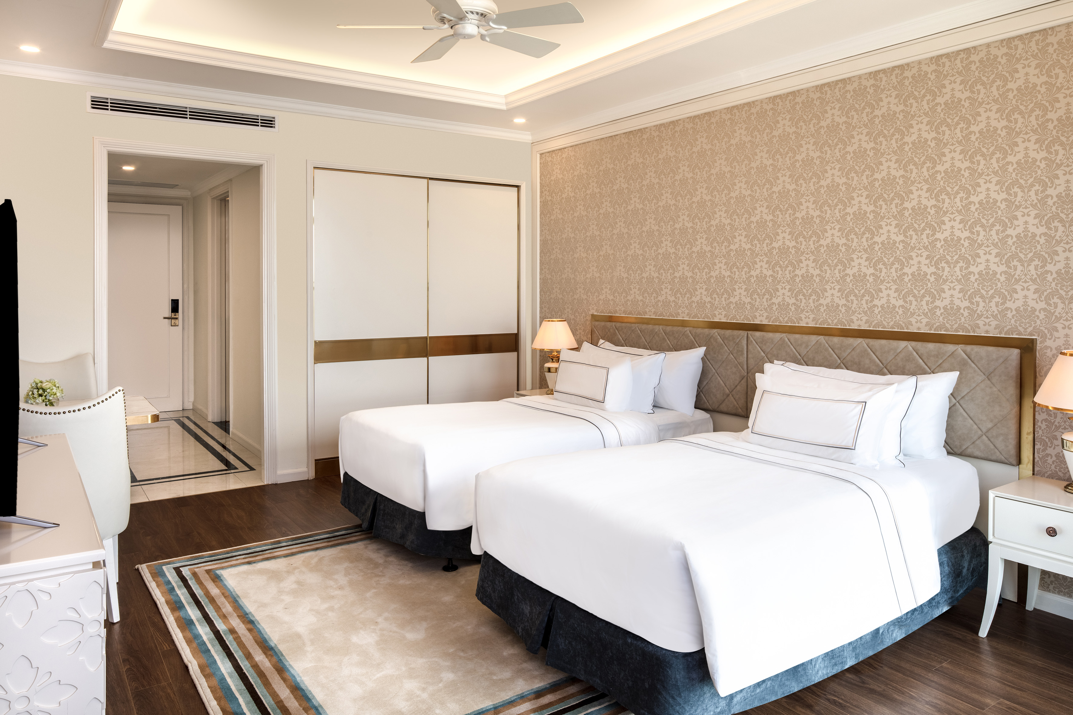 Hotel room with two twin beds, modern decor, patterned wallpaper, and wood floor.