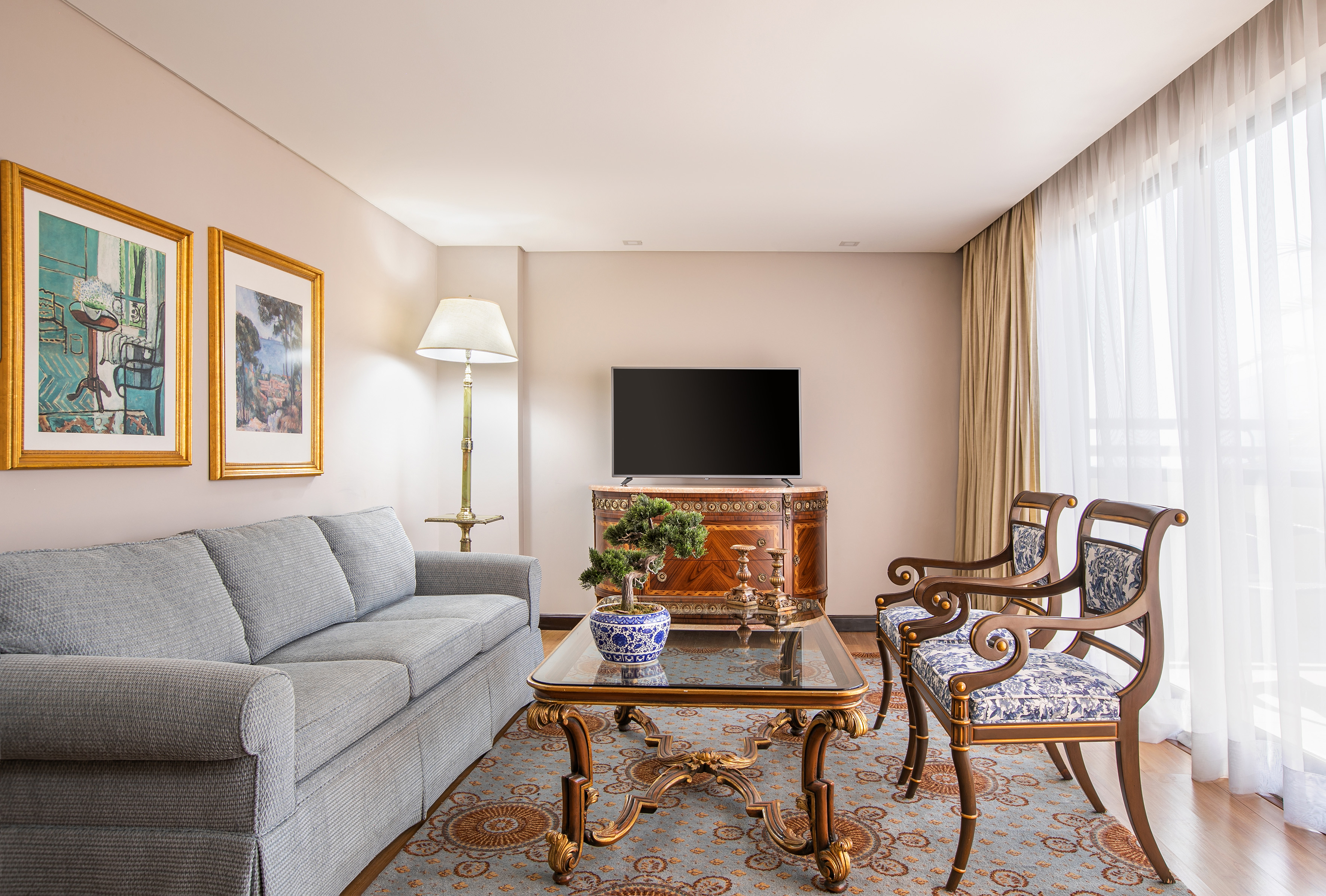 Classic elegant living room with gray sofa, ornate chairs, coffee table, TV, and art.