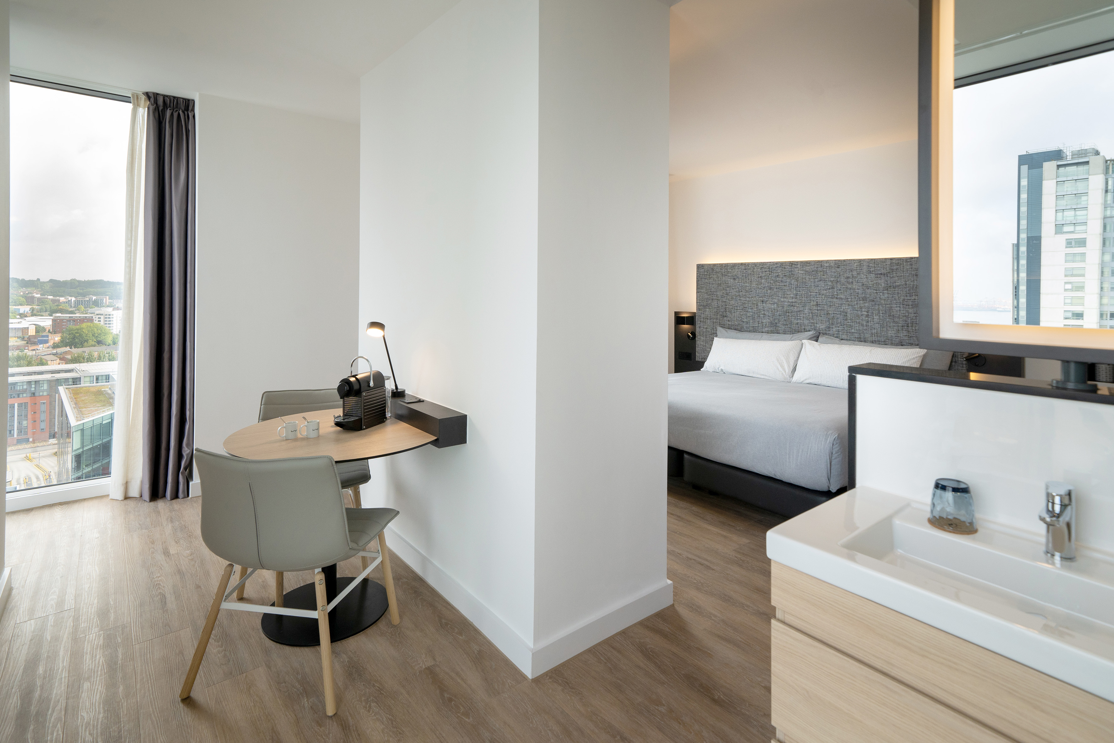 Modern hotel room with living area, Nespresso, bedroom, and city view.