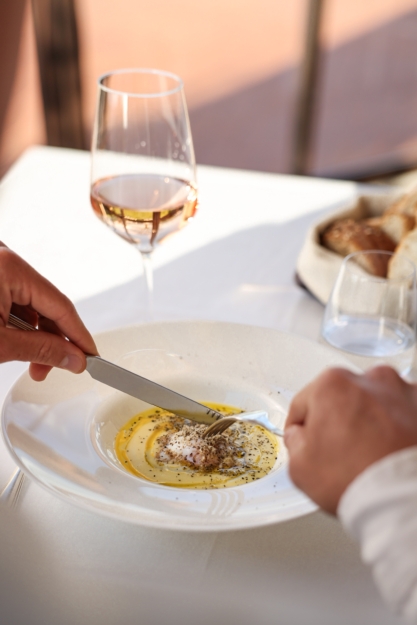 Hands cutting gourmet poached egg with truffle and pepper; rosé wine nearby.