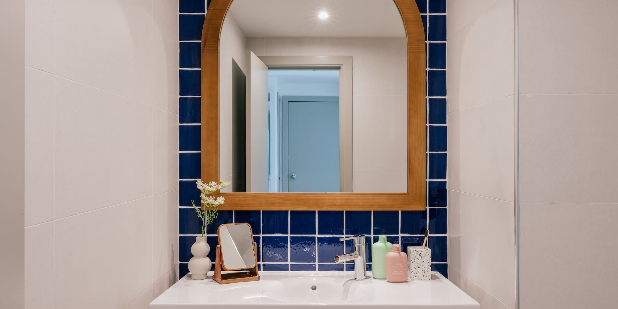 Modern bathroom with white vanity, arched wooden mirror, and blue square tiles.