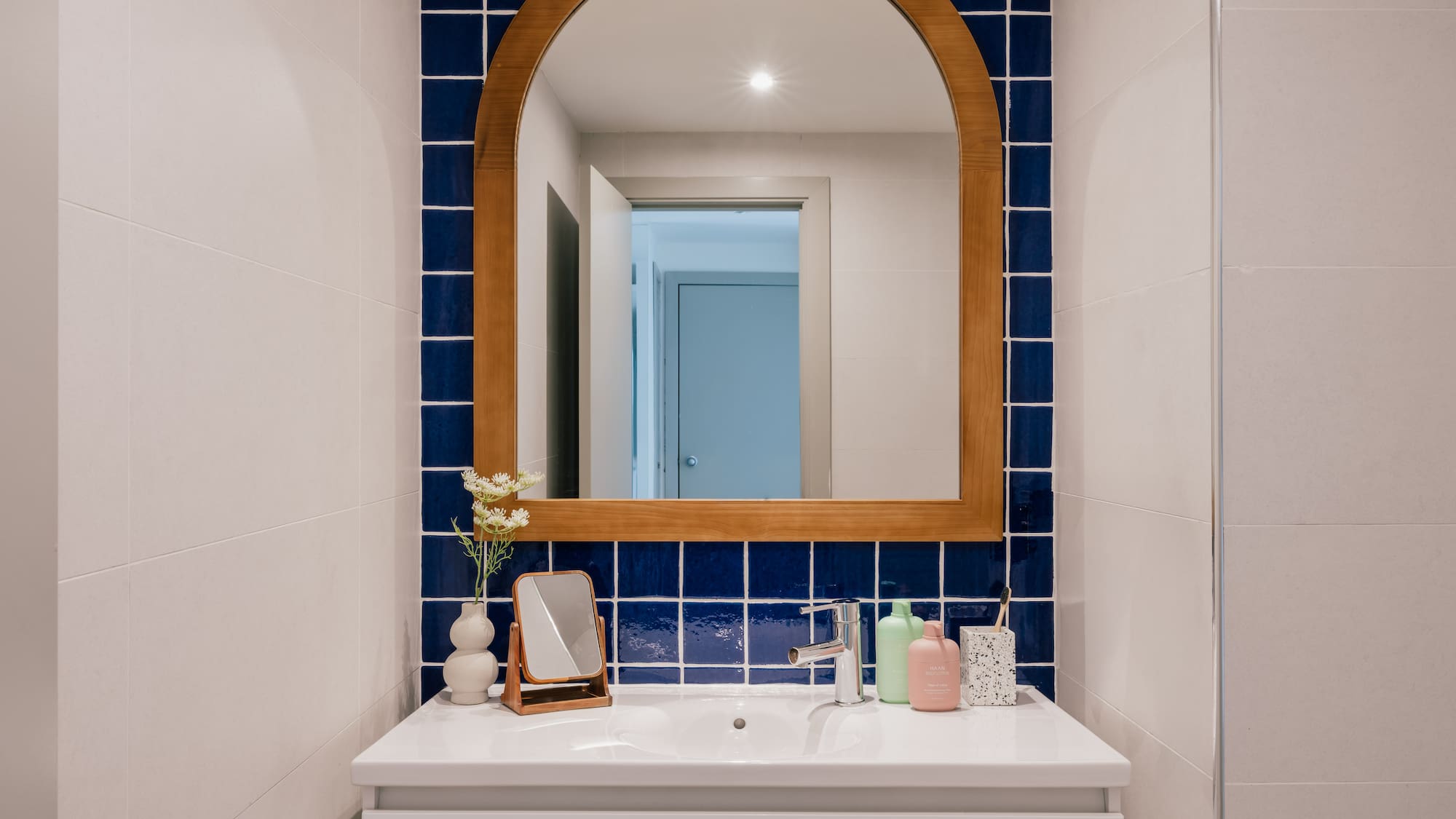 Modern bathroom with white vanity, arched wooden mirror, and blue square tiles.