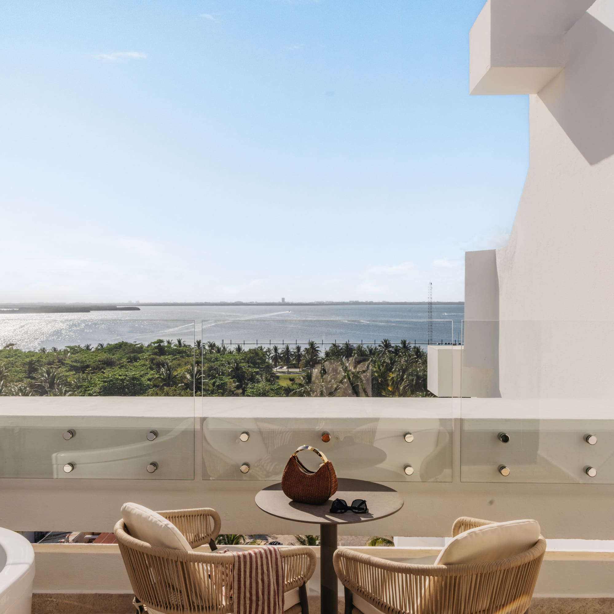 Luxury balcony with ocean view, outdoor bathtub, and tropical resort.