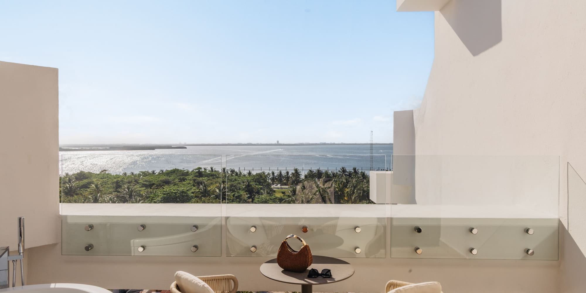Luxury balcony with ocean view, outdoor bathtub, and tropical resort.