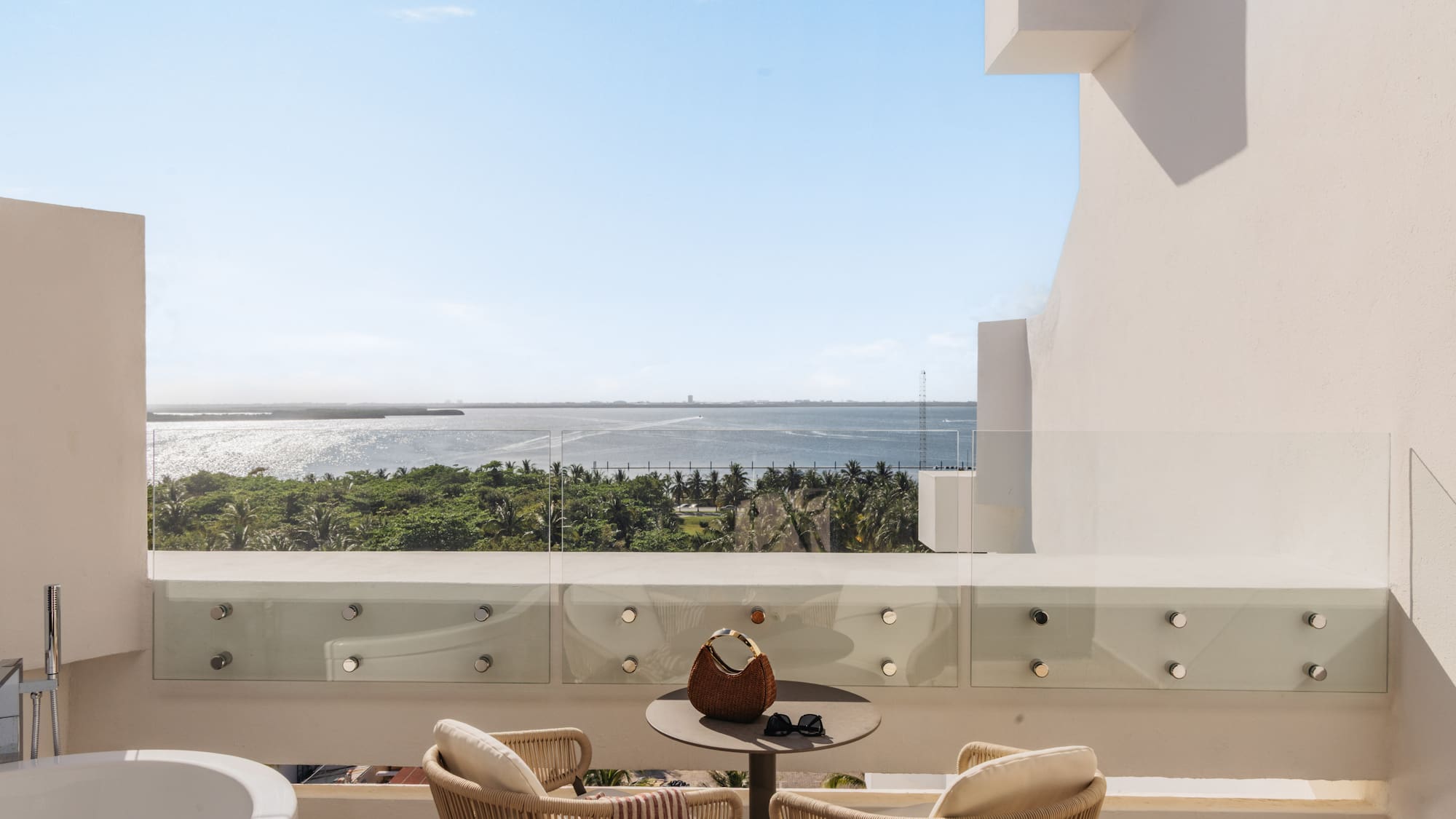 Luxury balcony with ocean view, outdoor bathtub, and tropical resort.