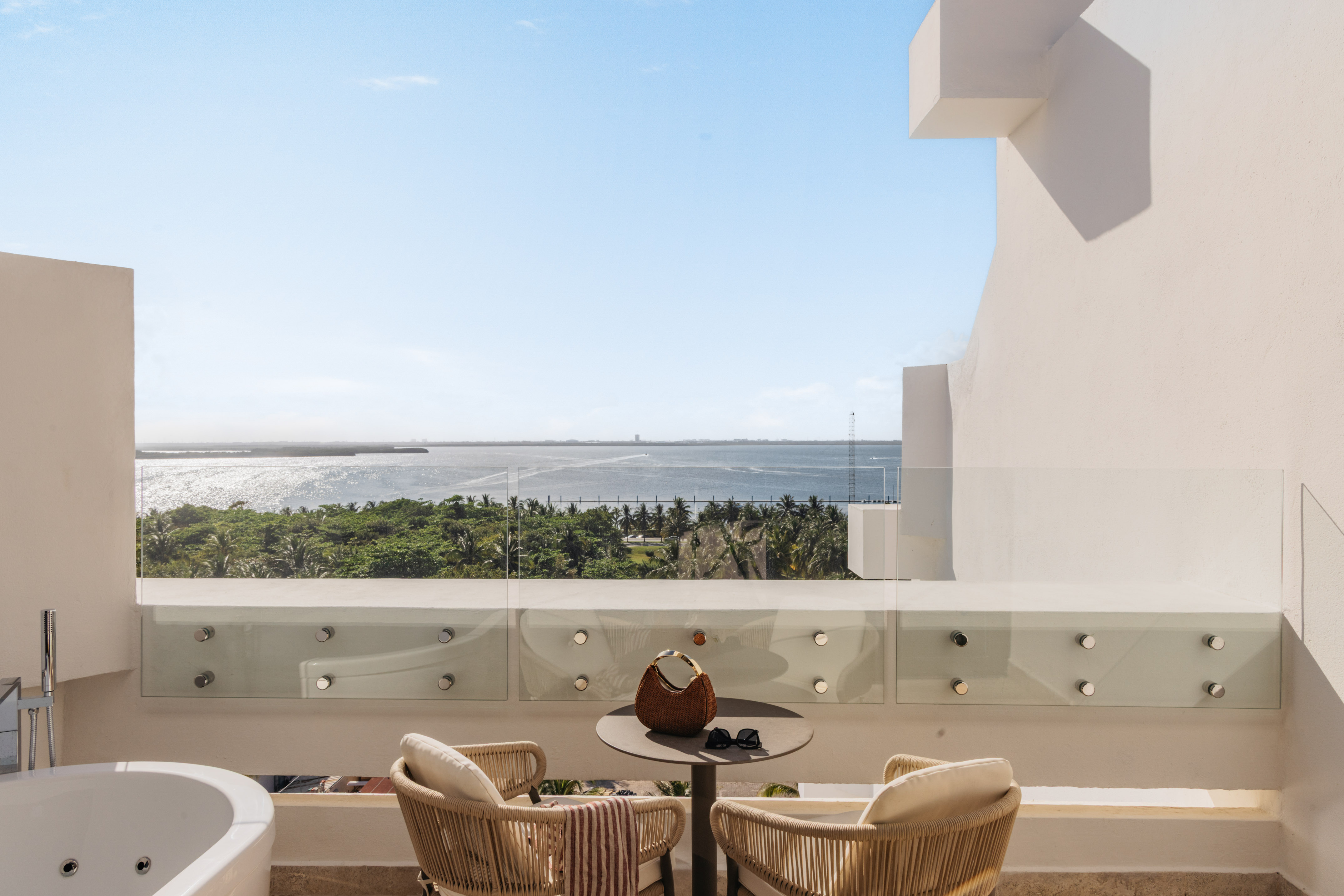 Luxury balcony with ocean view, outdoor bathtub, and tropical resort.