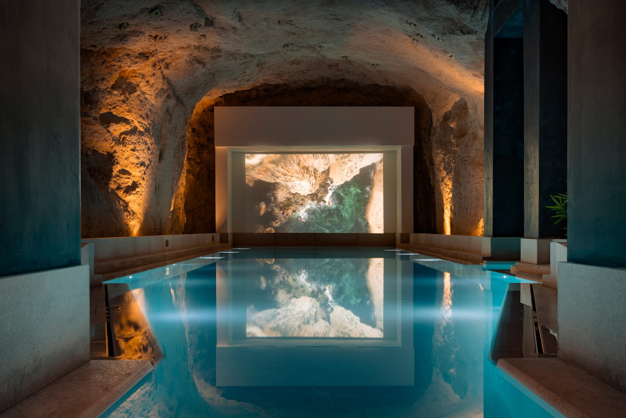 Indoor cavern pool with ambient lighting and coastal projection screen.