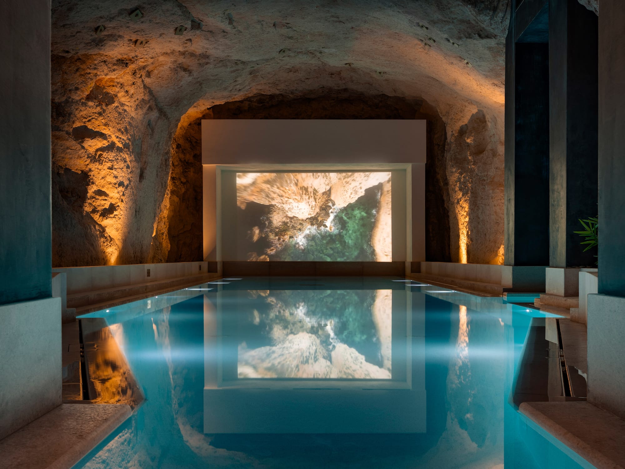 Indoor cavern pool with ambient lighting and coastal projection screen.
