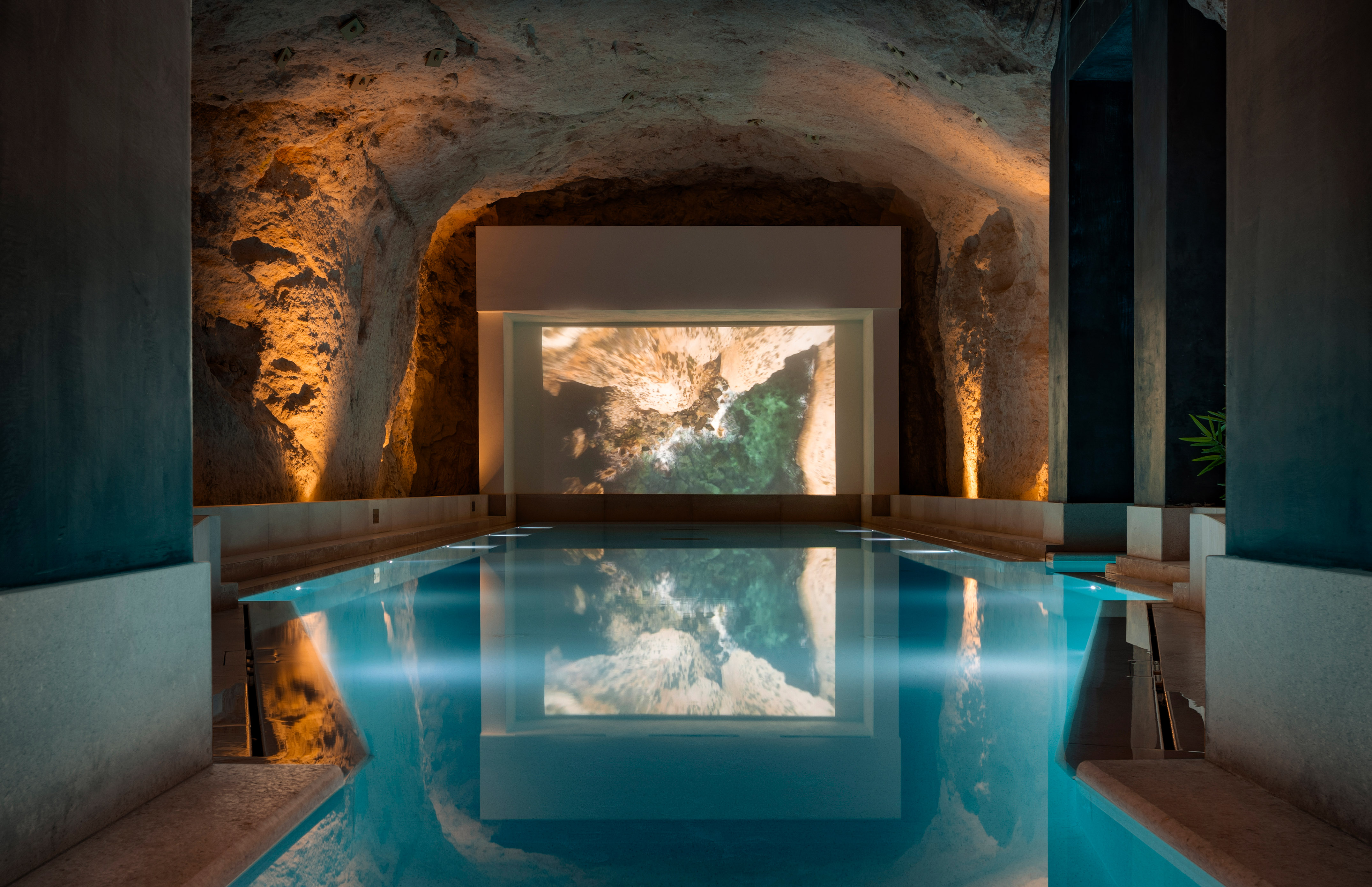 Indoor cavern pool with ambient lighting and coastal projection screen.