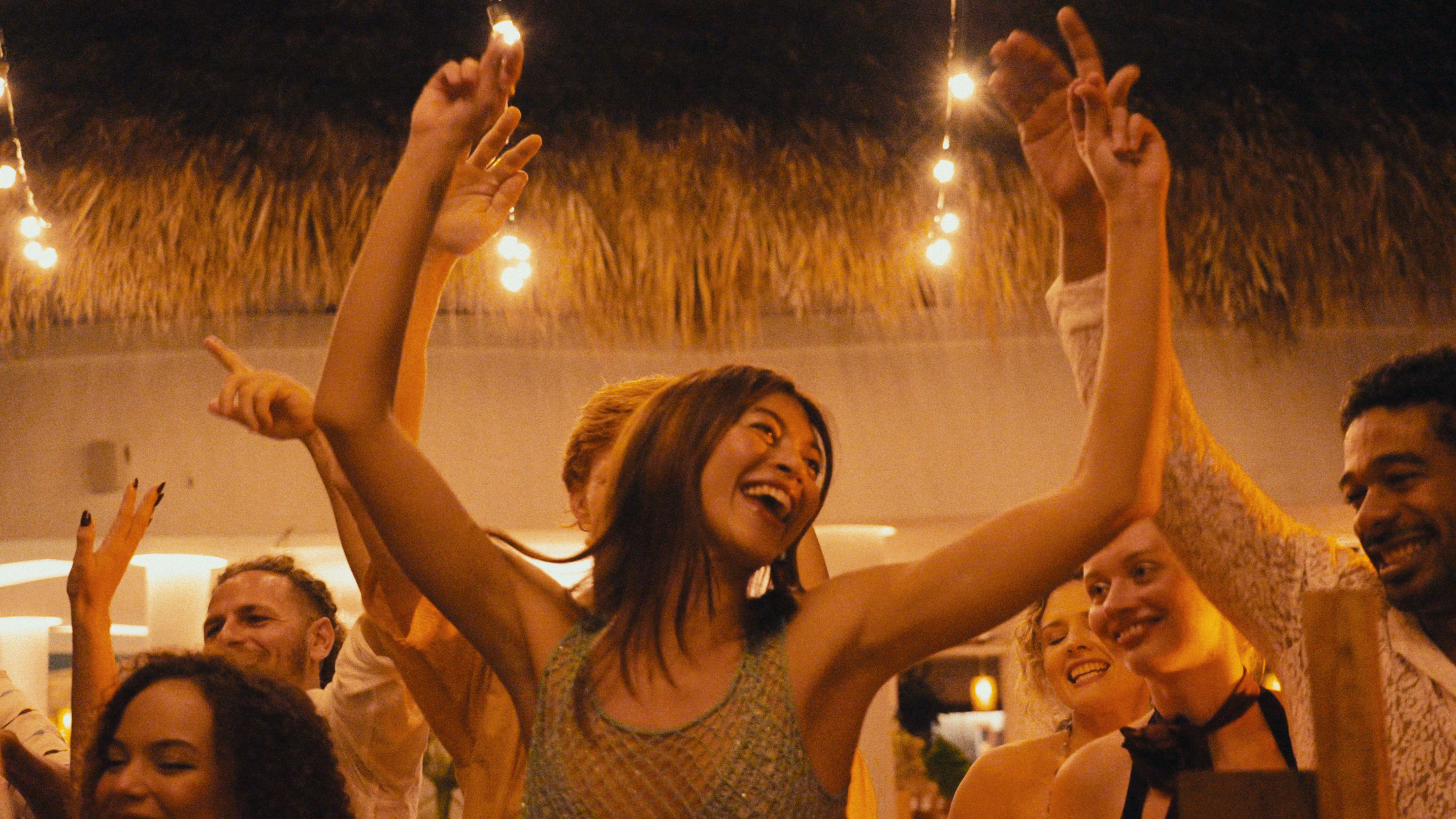 Smiling woman dancing with friends at an outdoor night party with lights.