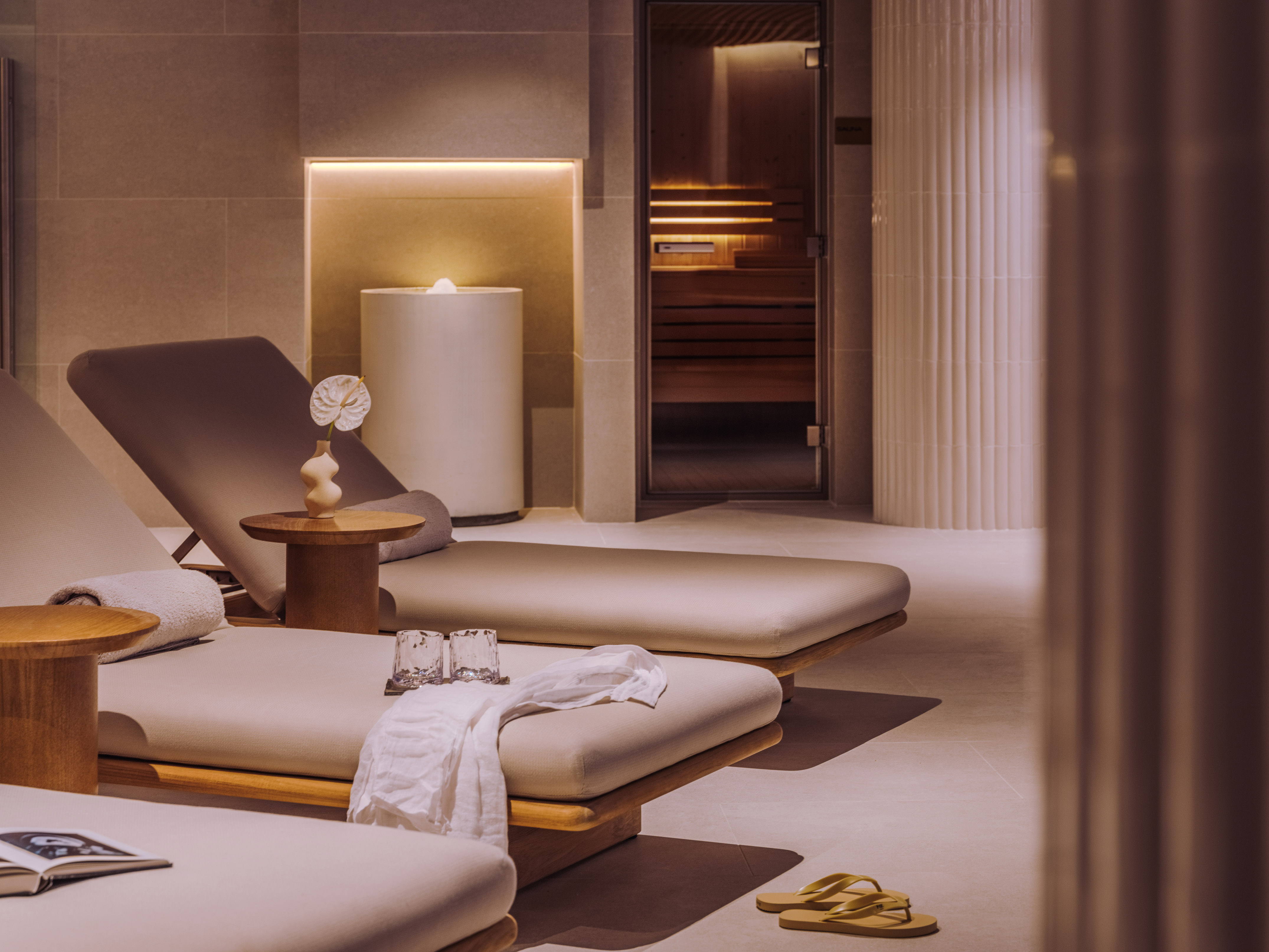 Serene spa relaxation lounge with elegant chaise lounges and a sauna entrance.