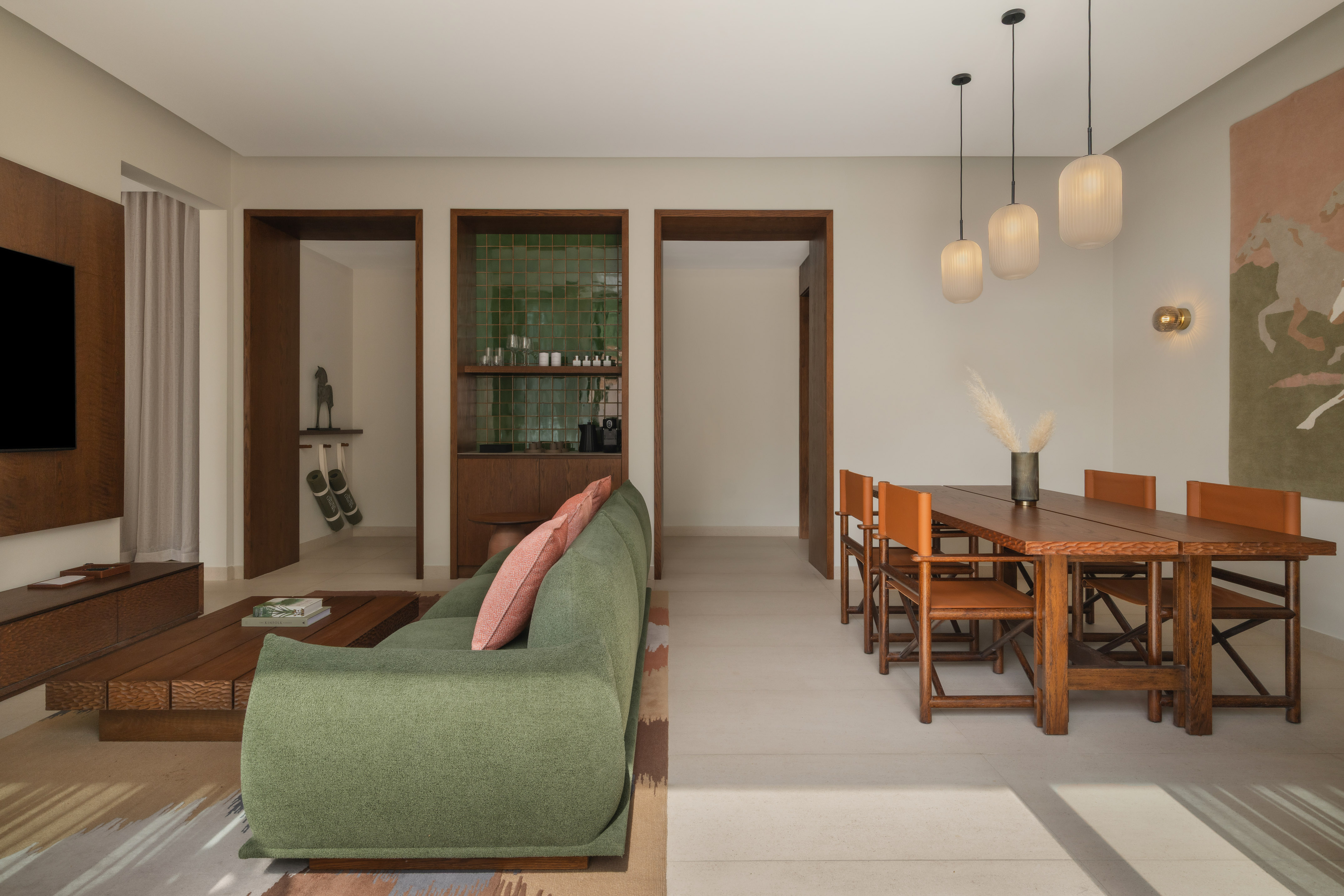 Open plan living and dining area with green sofa, wooden table, and modern lights.