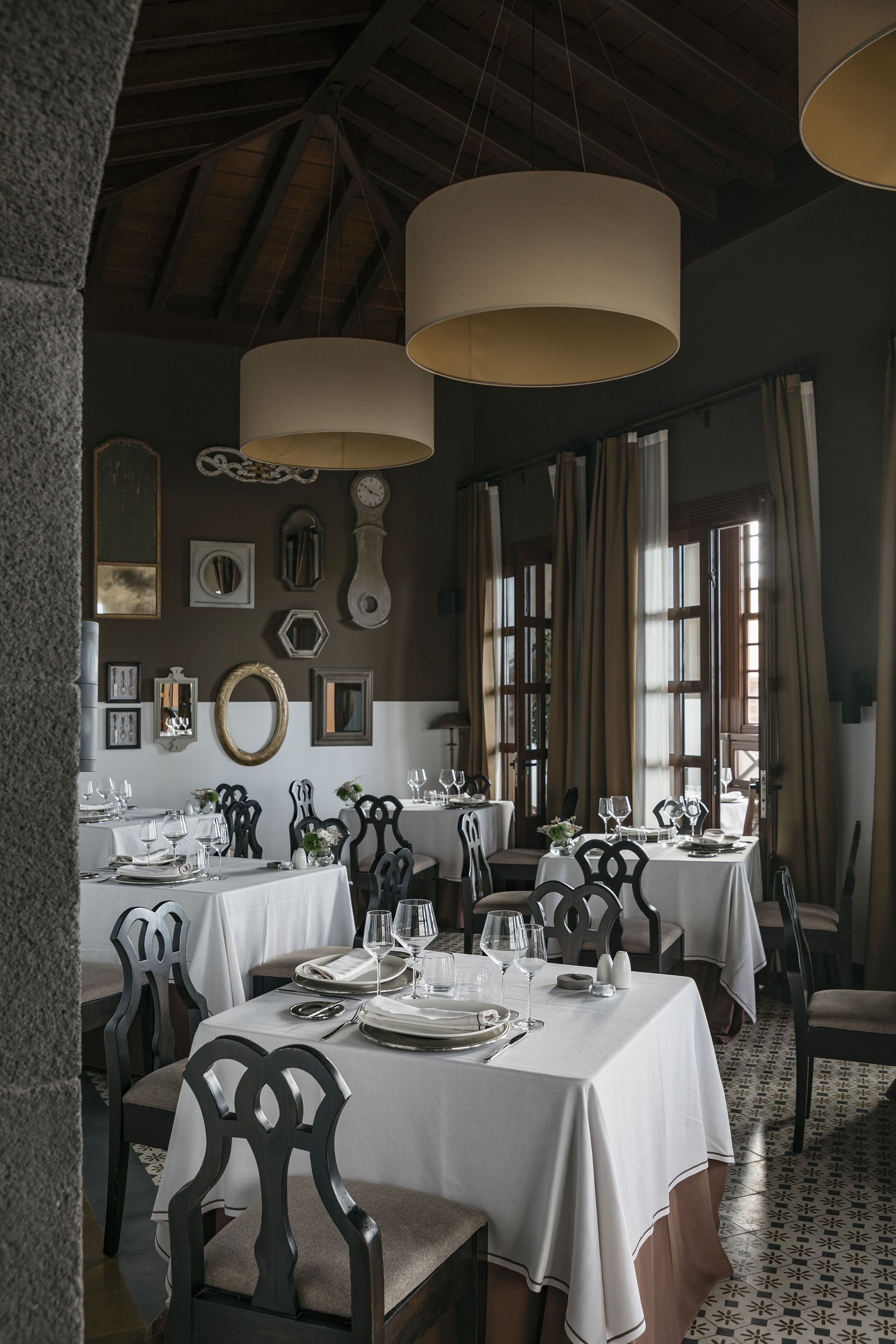 Elegant restaurant dining room with set tables, dark chairs, and ceiling lamps.
