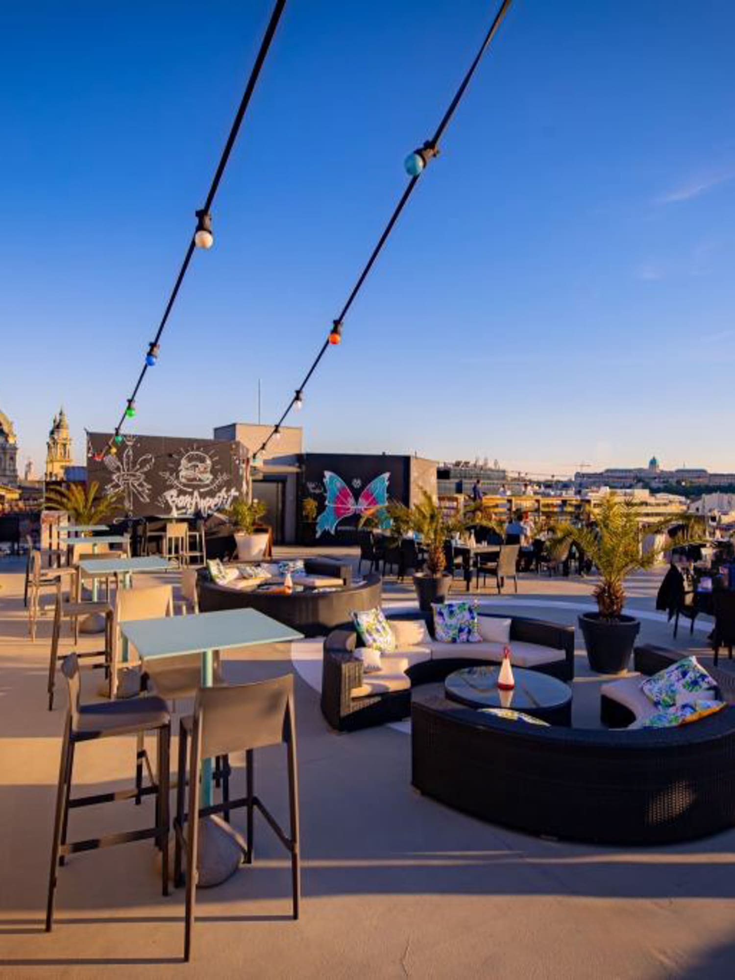 Rooftop bar with outdoor dining, lounge areas, city skyline, and sunset ambiance.