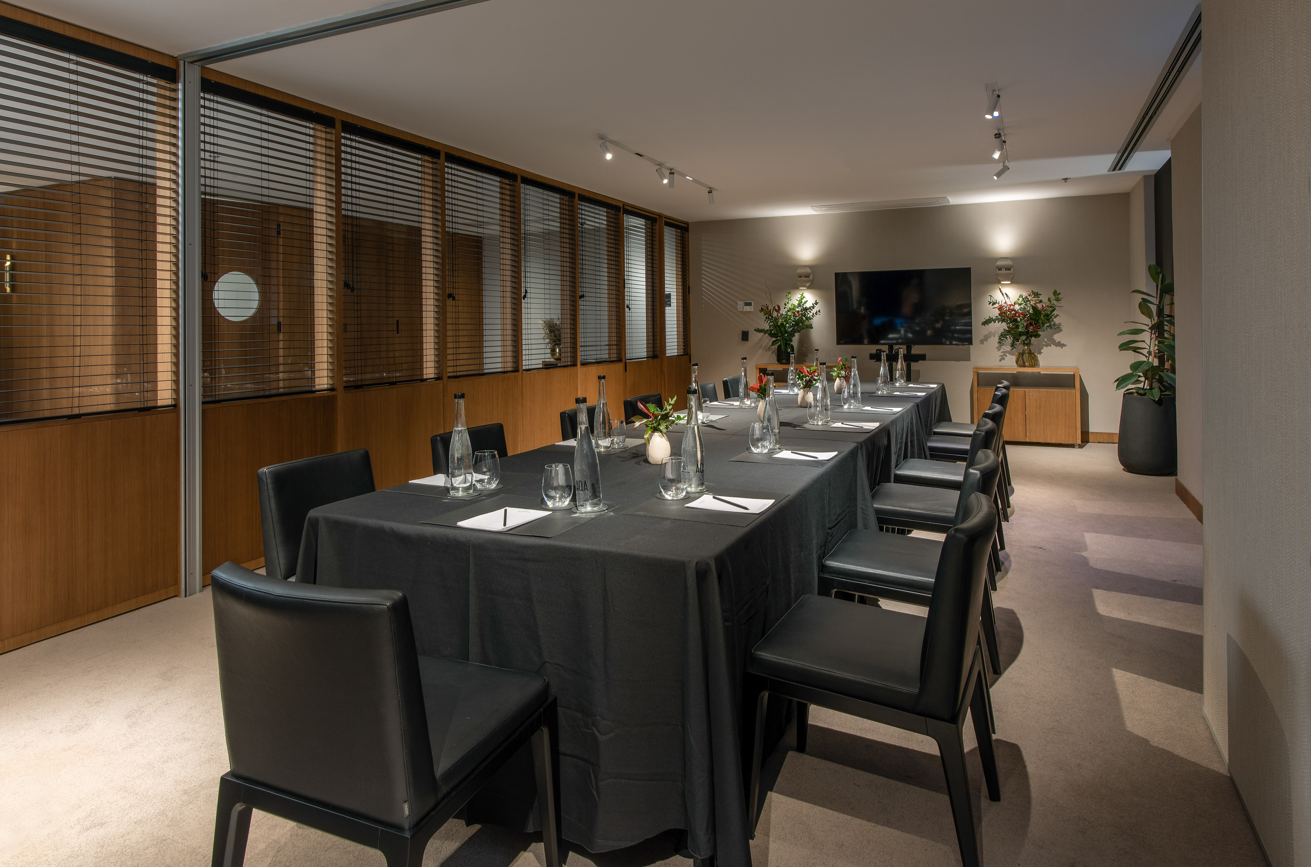 Modern boardroom with long black table, chairs, water bottles, and TV.