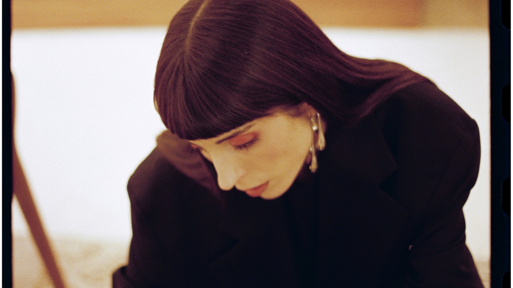 Mujer con blazer negro concentrada en revista de arte, piano borroso al fondo.
