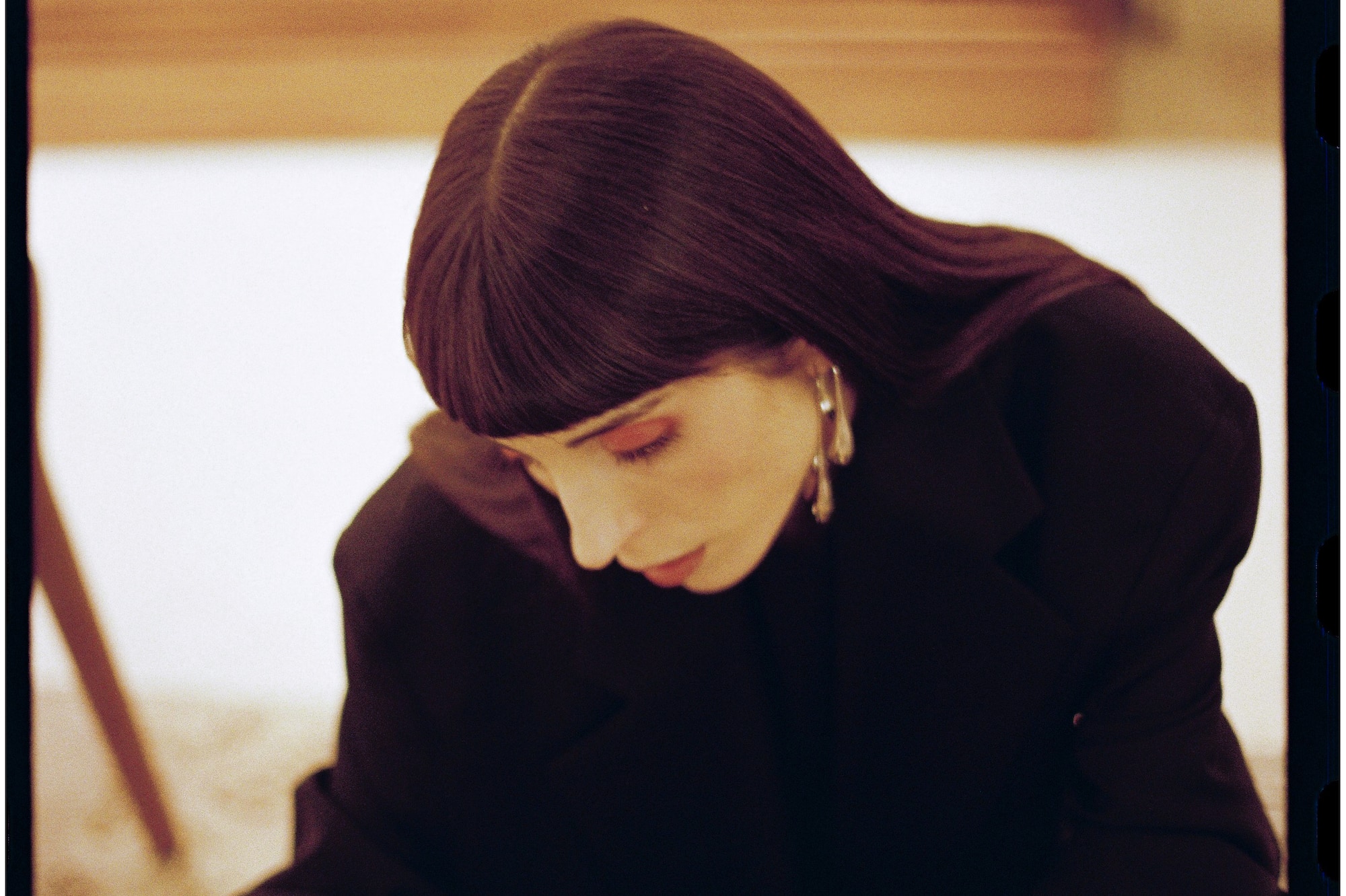 Mujer con blazer negro concentrada en revista de arte, piano borroso al fondo.