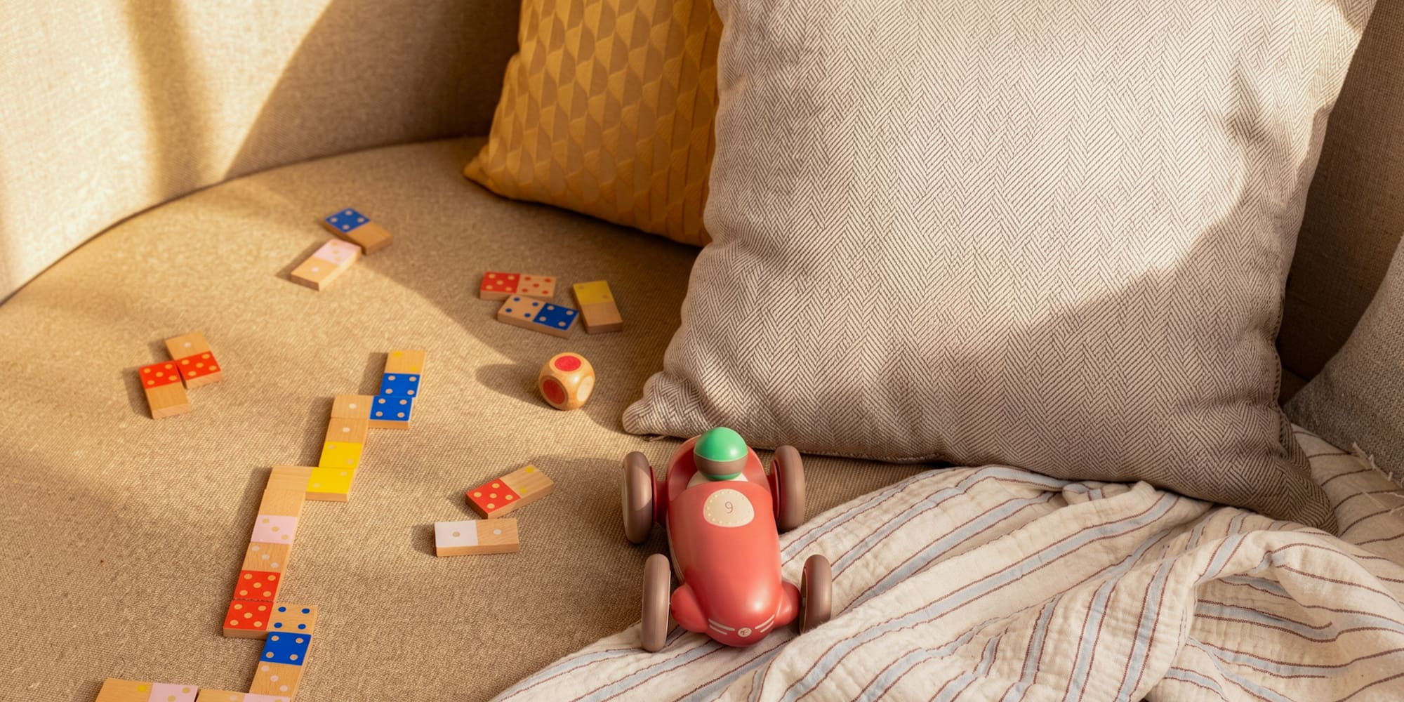 Kids' wooden dominoes, race car, and dice on a cozy sofa.