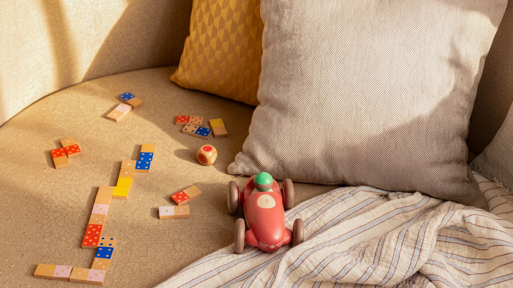 Kids' wooden dominoes, race car, and dice on a cozy sofa.