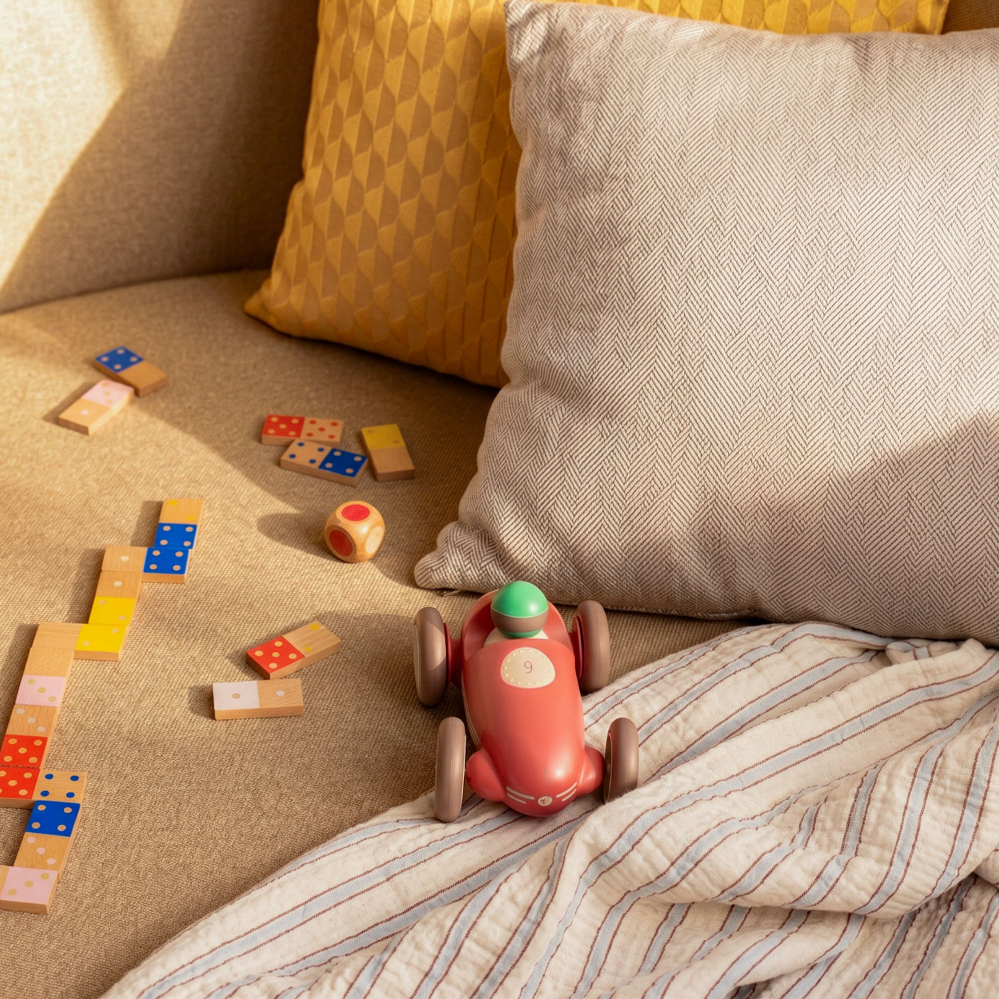 Kids' wooden dominoes, race car, and dice on a cozy sofa.