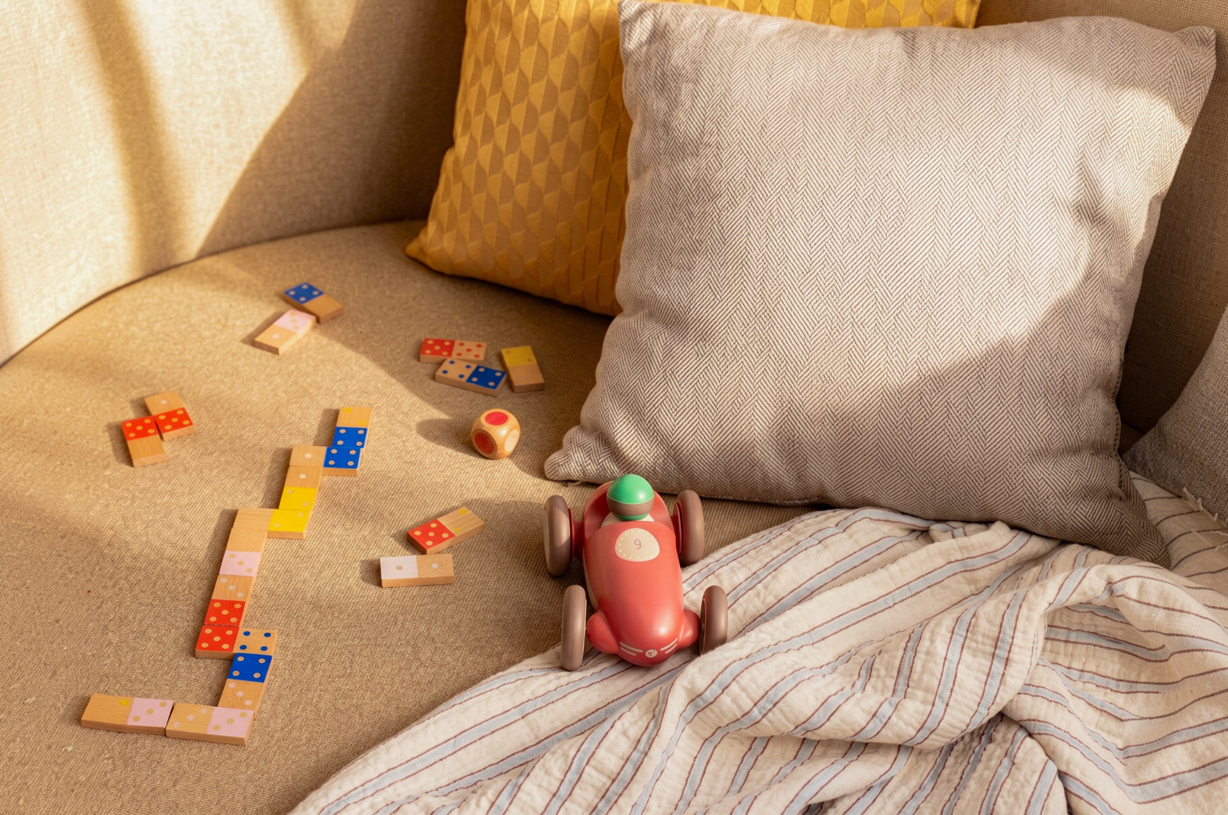 Kids' wooden dominoes, race car, and dice on a cozy sofa.