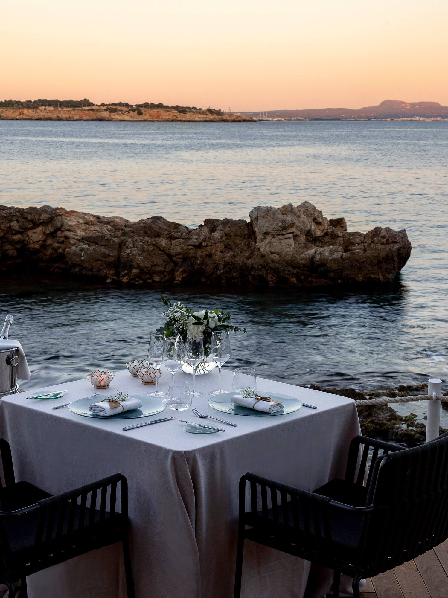 Cena romántica con champán frente al mar al atardecer.