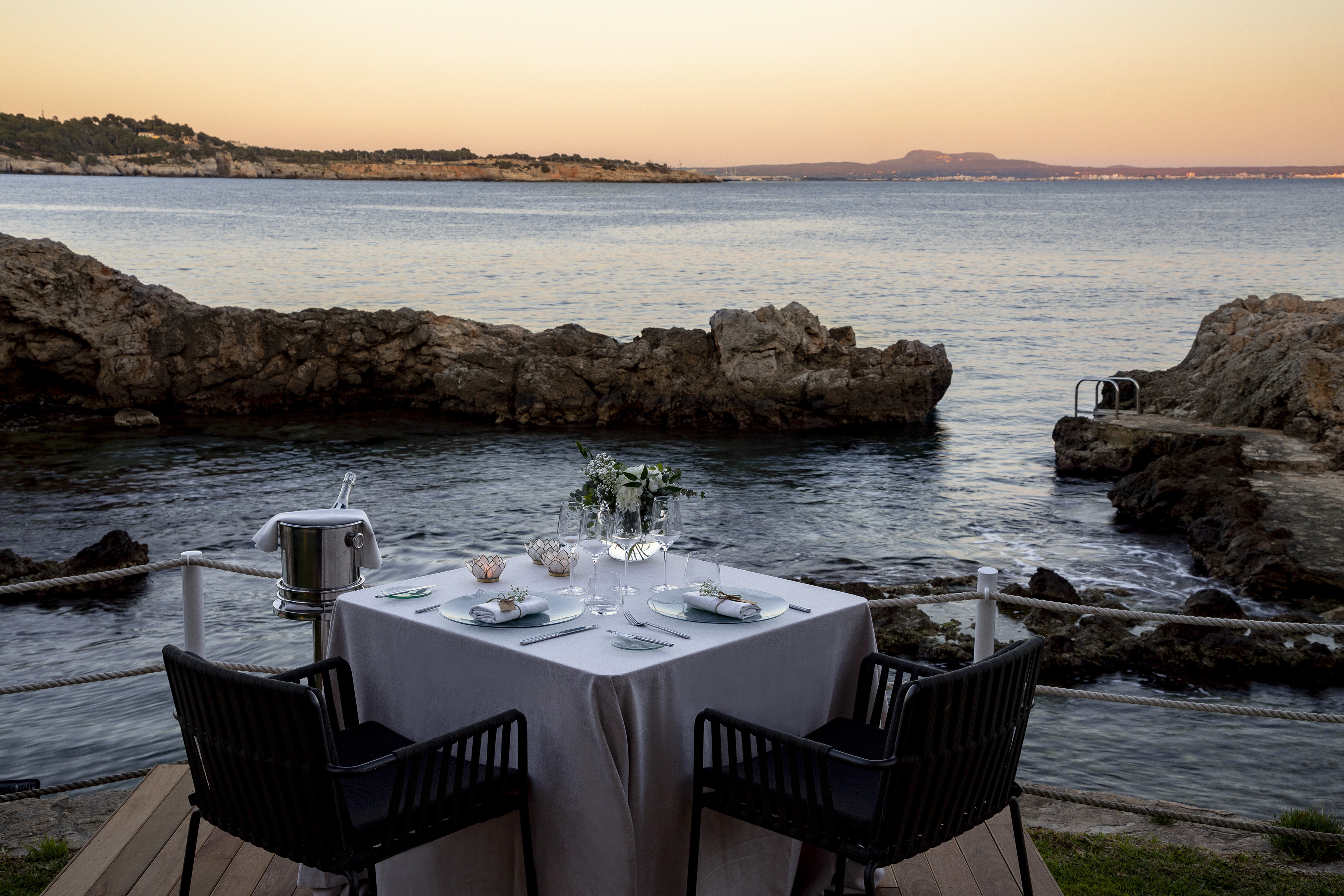 Cena romántica con champán frente al mar al atardecer.