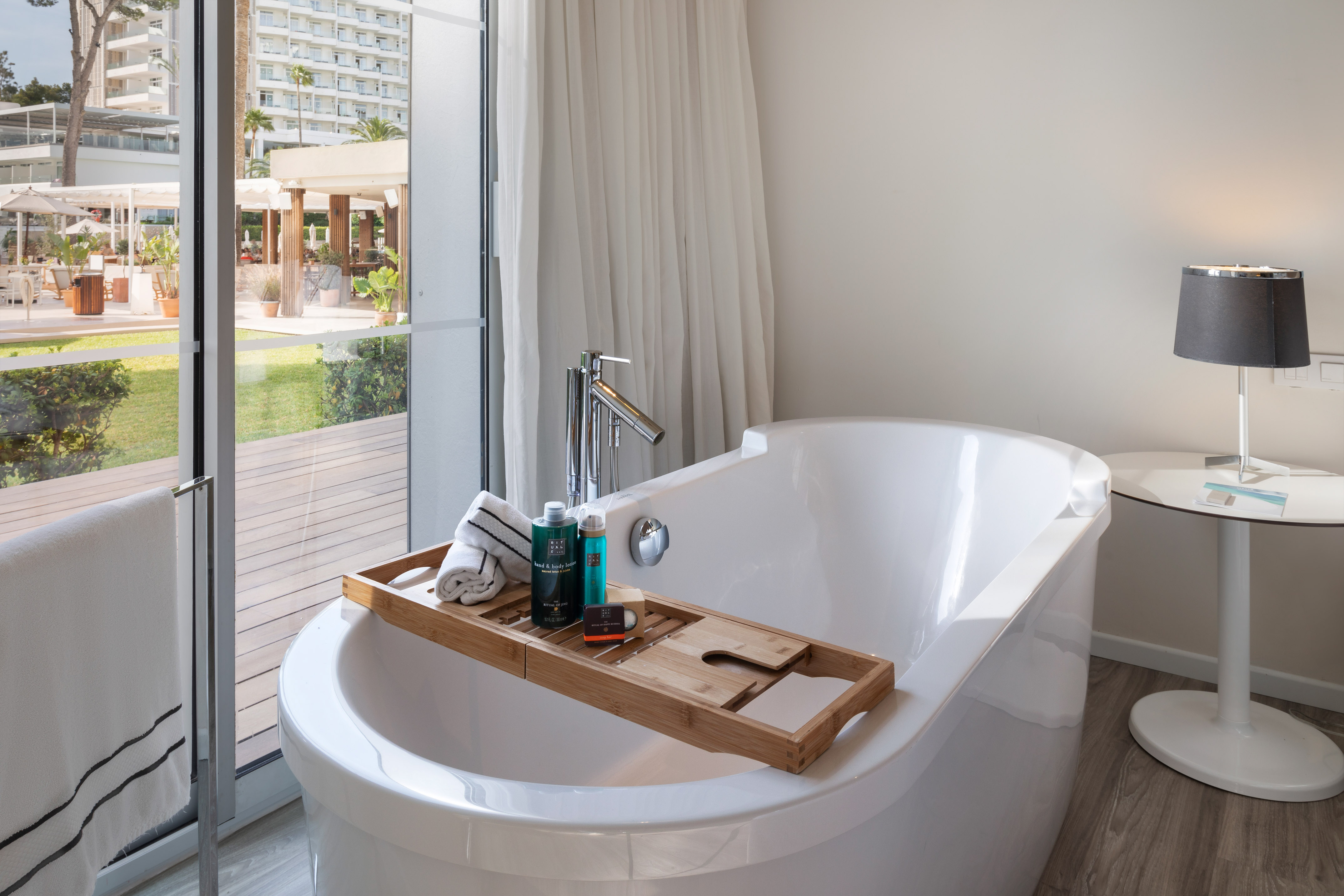 Modern white bathtub with bath caddy overlooking a resort garden view from window.