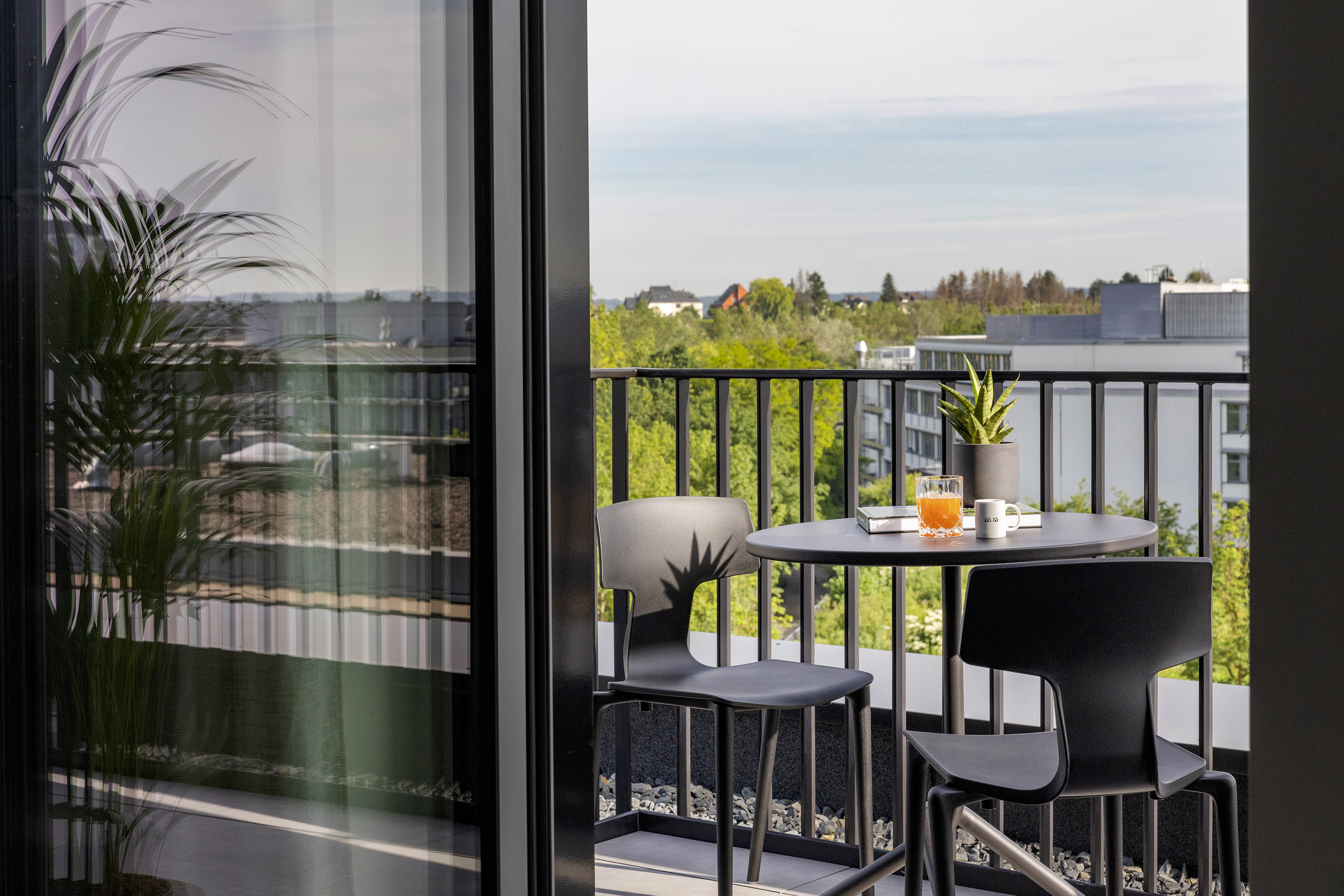 Urban balcony with black bistro set, orange juice, and city view.