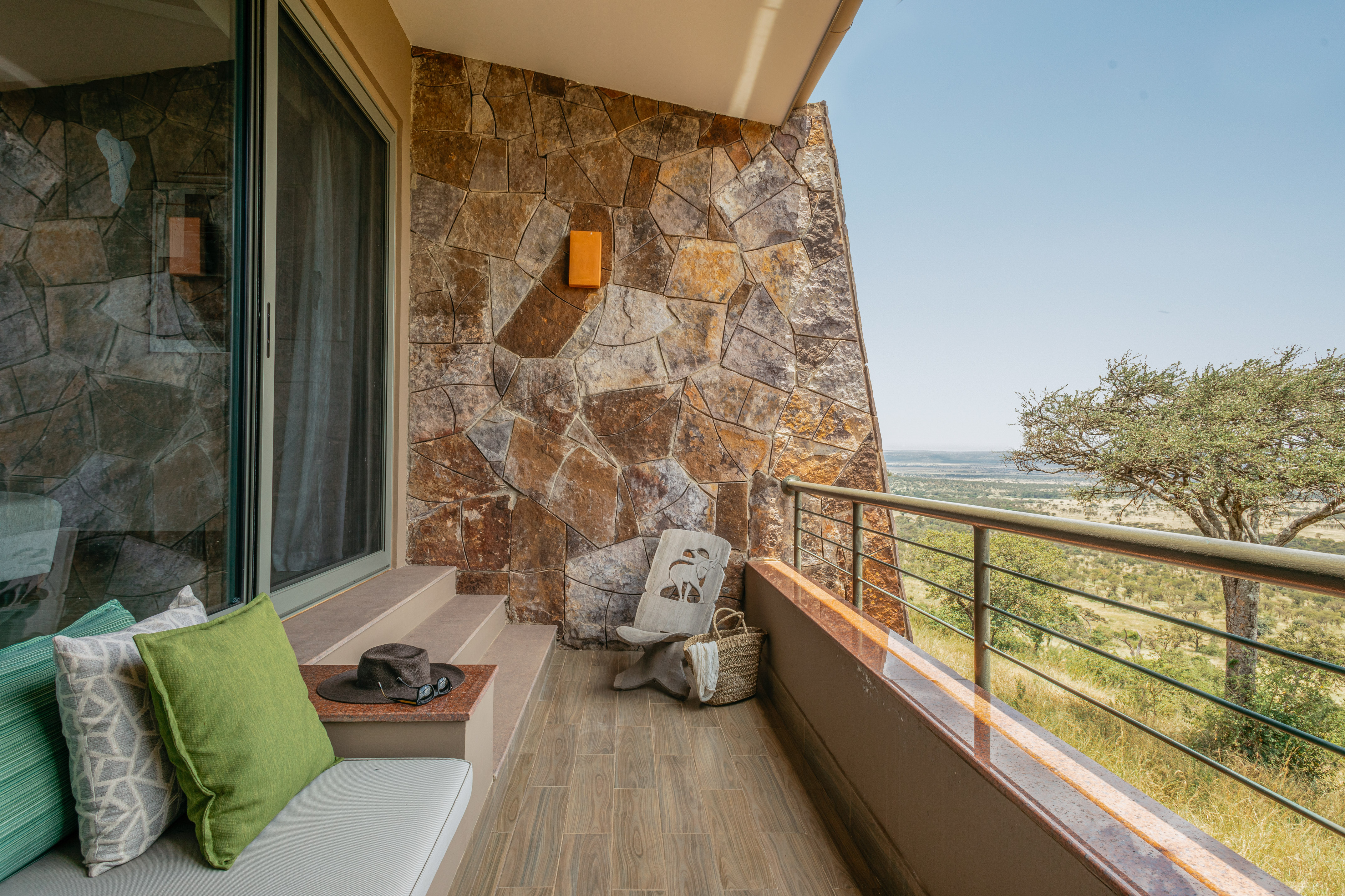 Balcony at African safari lodge overlooking savanna, stone wall, outdoor seating.