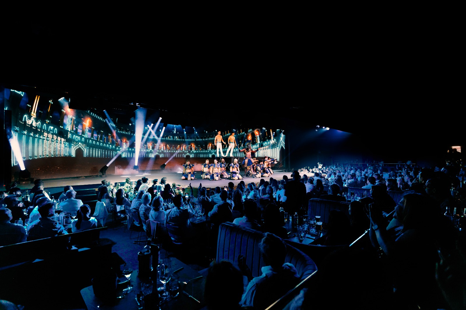 Live stage show with performers, architectural backdrop, and audience.