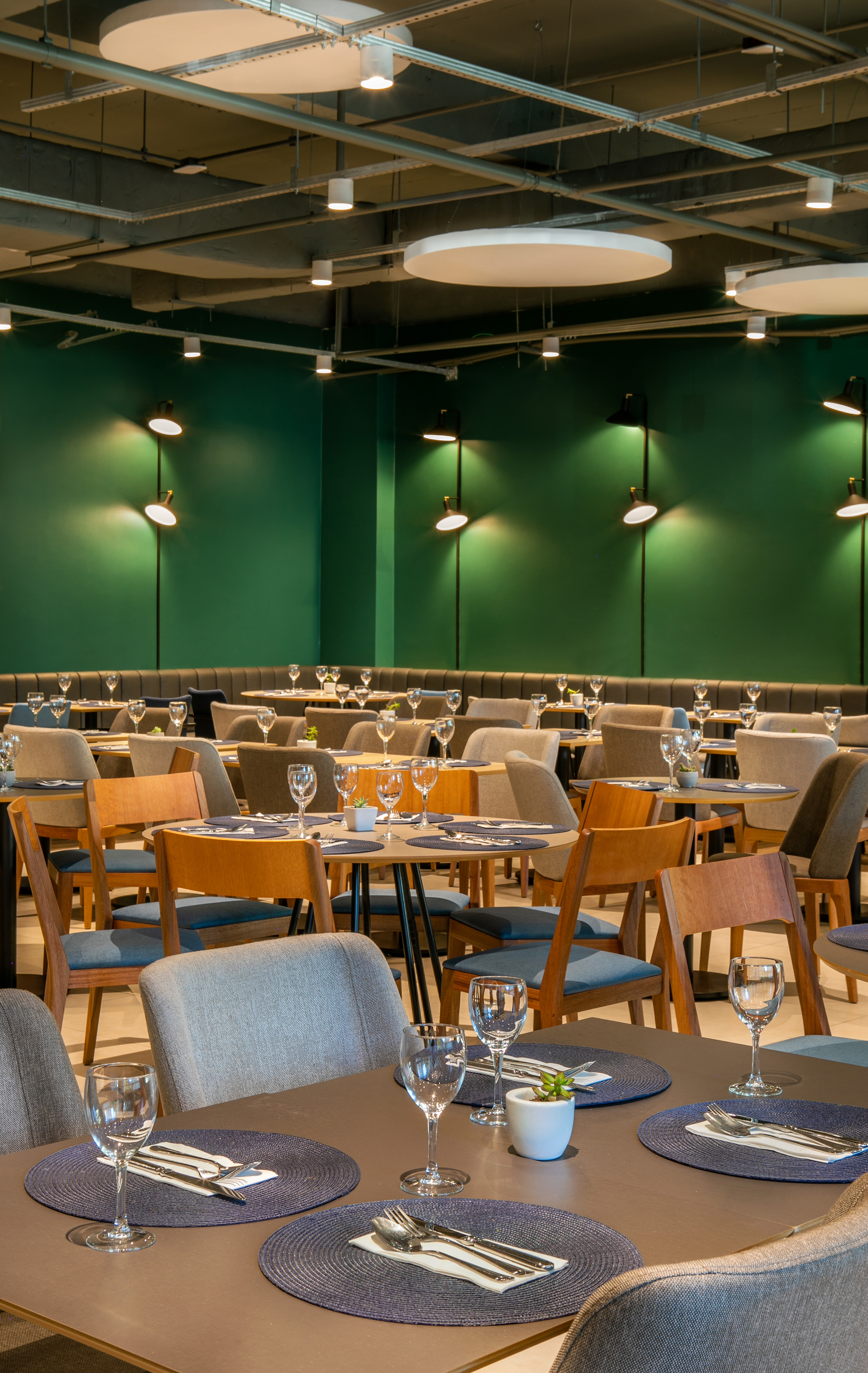 Modern restaurant dining room with green walls, set tables, and industrial ceiling.